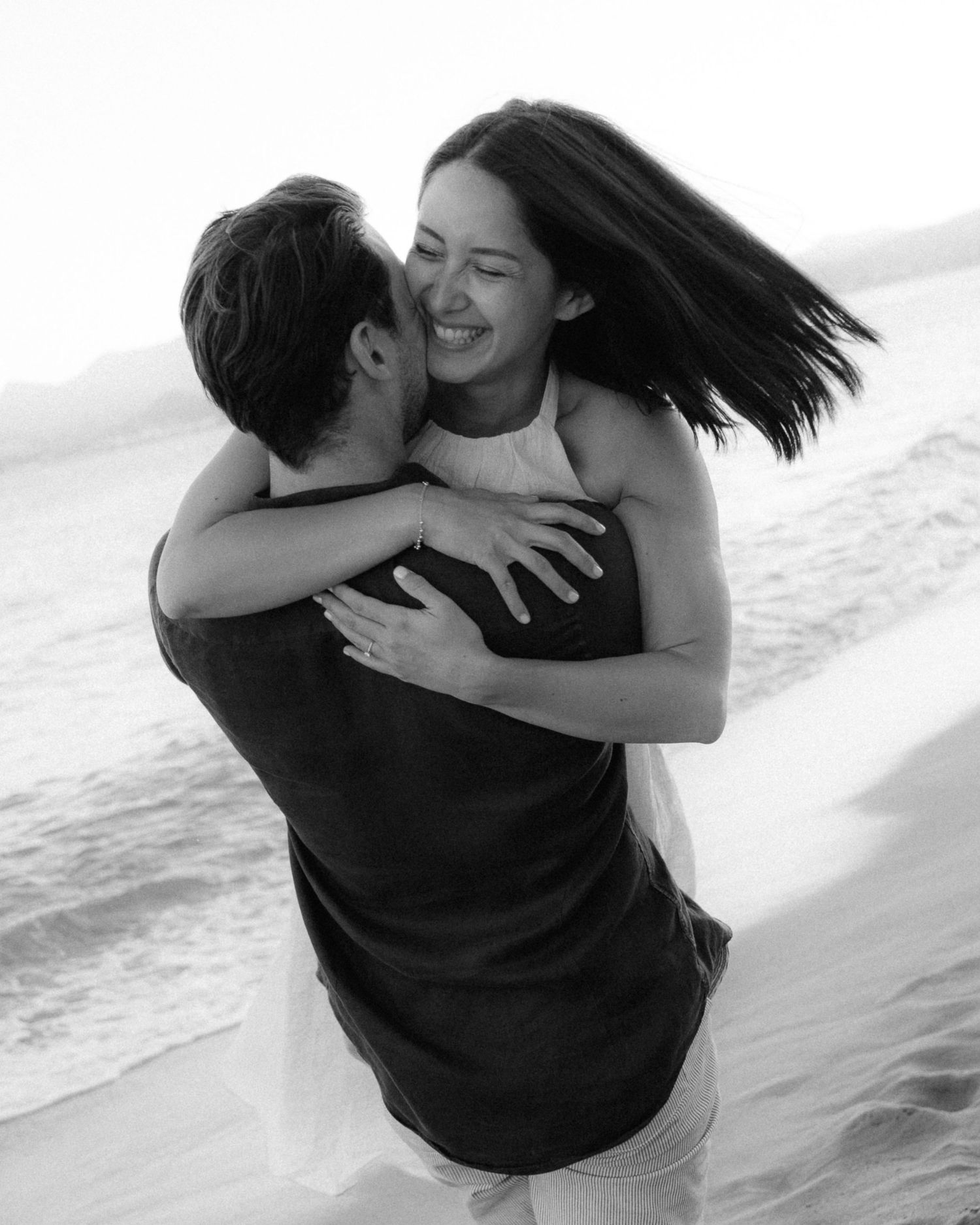 A romantic black and white photo series of a couple embracing and spinning on a beach.