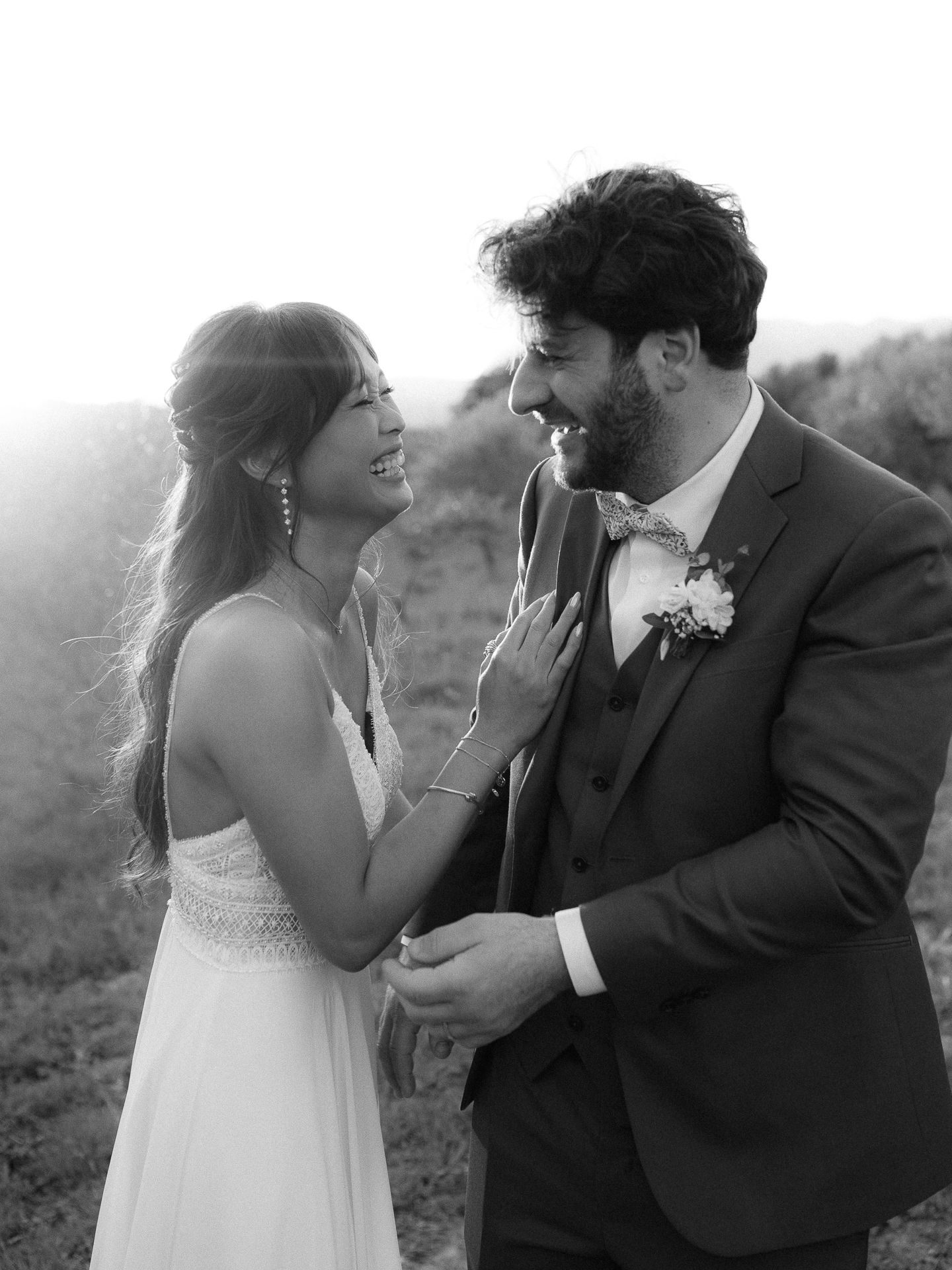 Black and white wedding photo of smiling bride and groom sharing a joyful moment outdoors.
