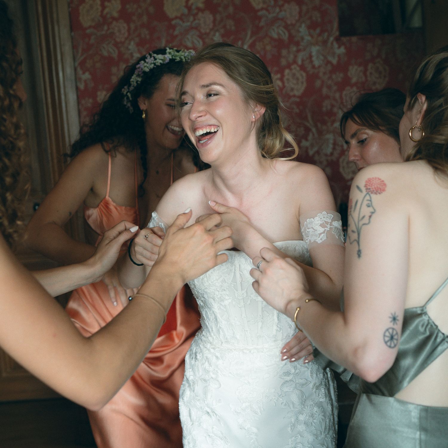 Bride in white dress laughing joyfully with wedding guests during a candid reception moment.