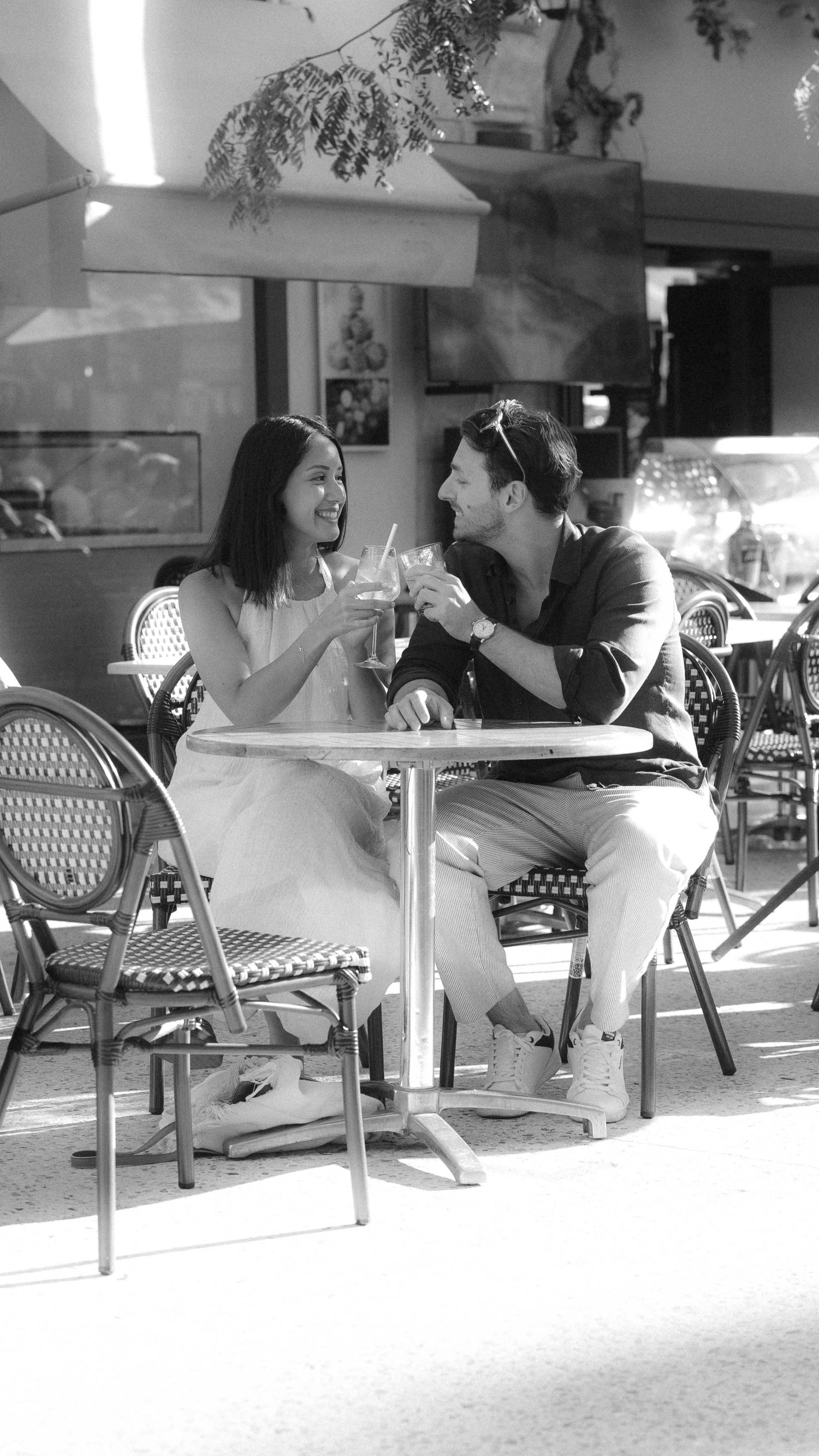 A couple enjoys drinks together at an outdoor cafe table on a sunny afternoon.