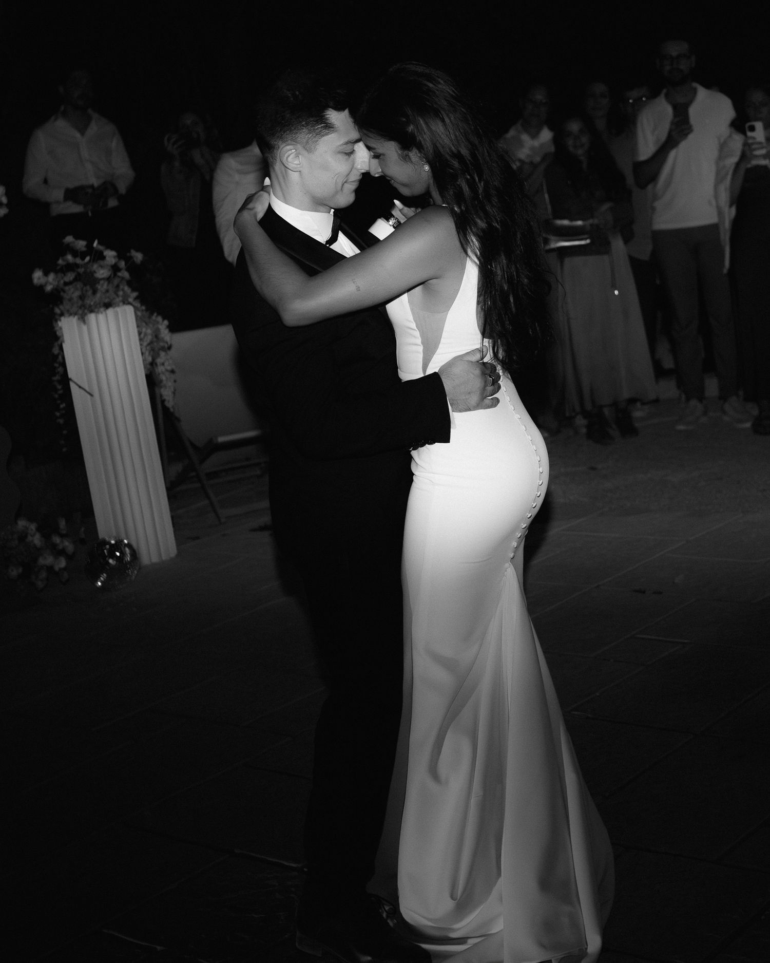 A couple shares a romantic dance together at a wedding reception, with the bride in a white gown and guests in the background.