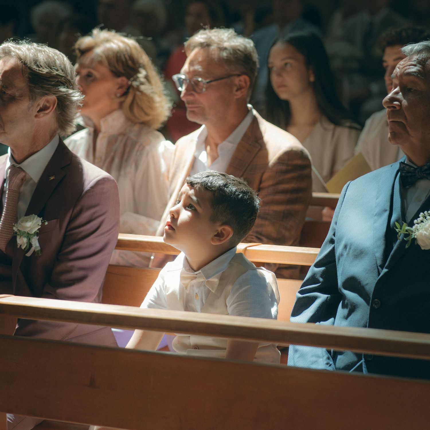 People sitting in wooden pews listen attentively during what appears to be a church service or gathering.