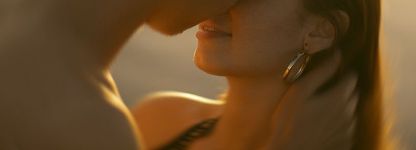 A person with long dark hair and red lipstick poses against a warm-toned background in a close-up beauty shot.