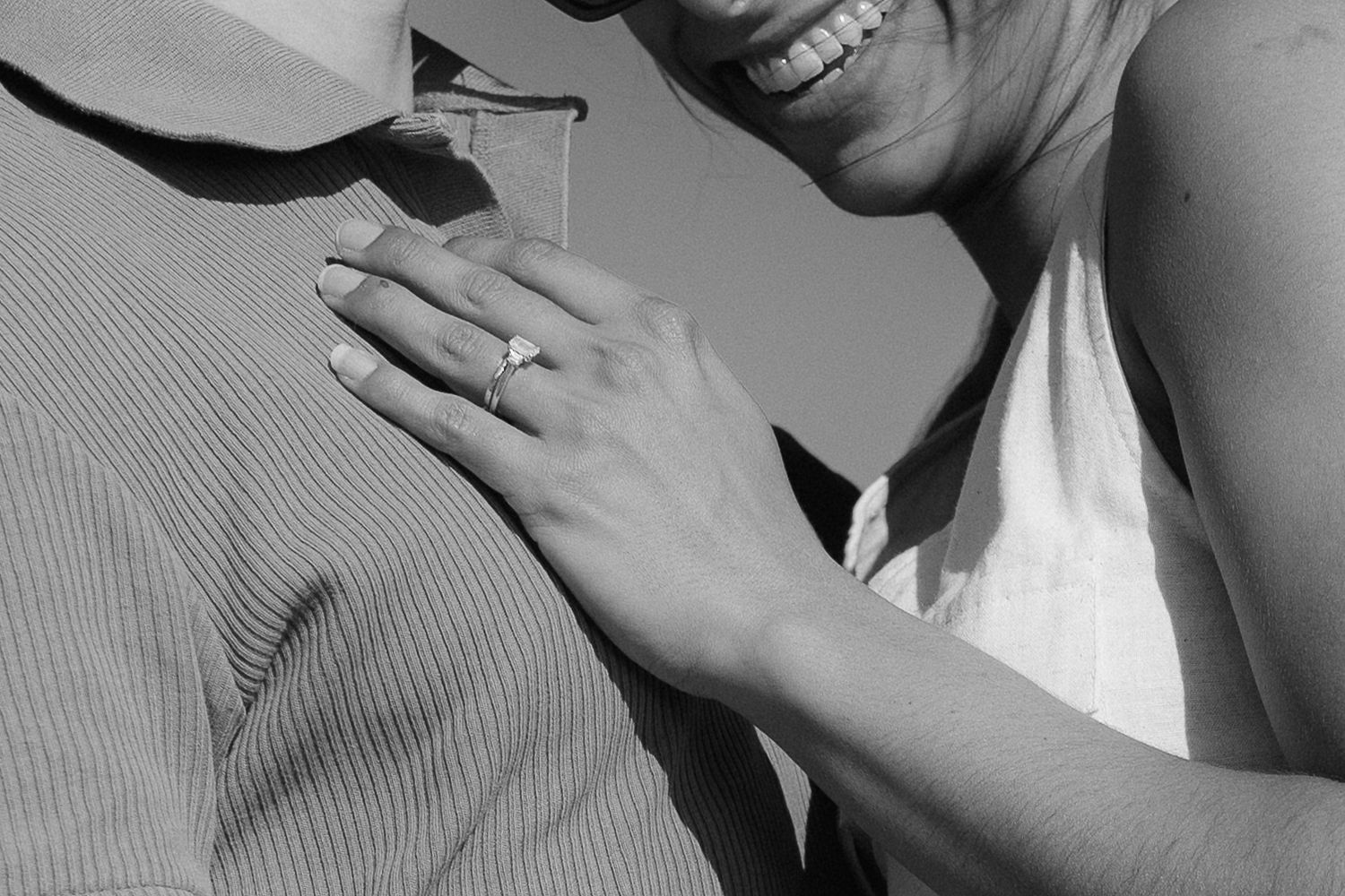 A person smiling while wearing a gray sweater and white shirt in a black and white photograph.