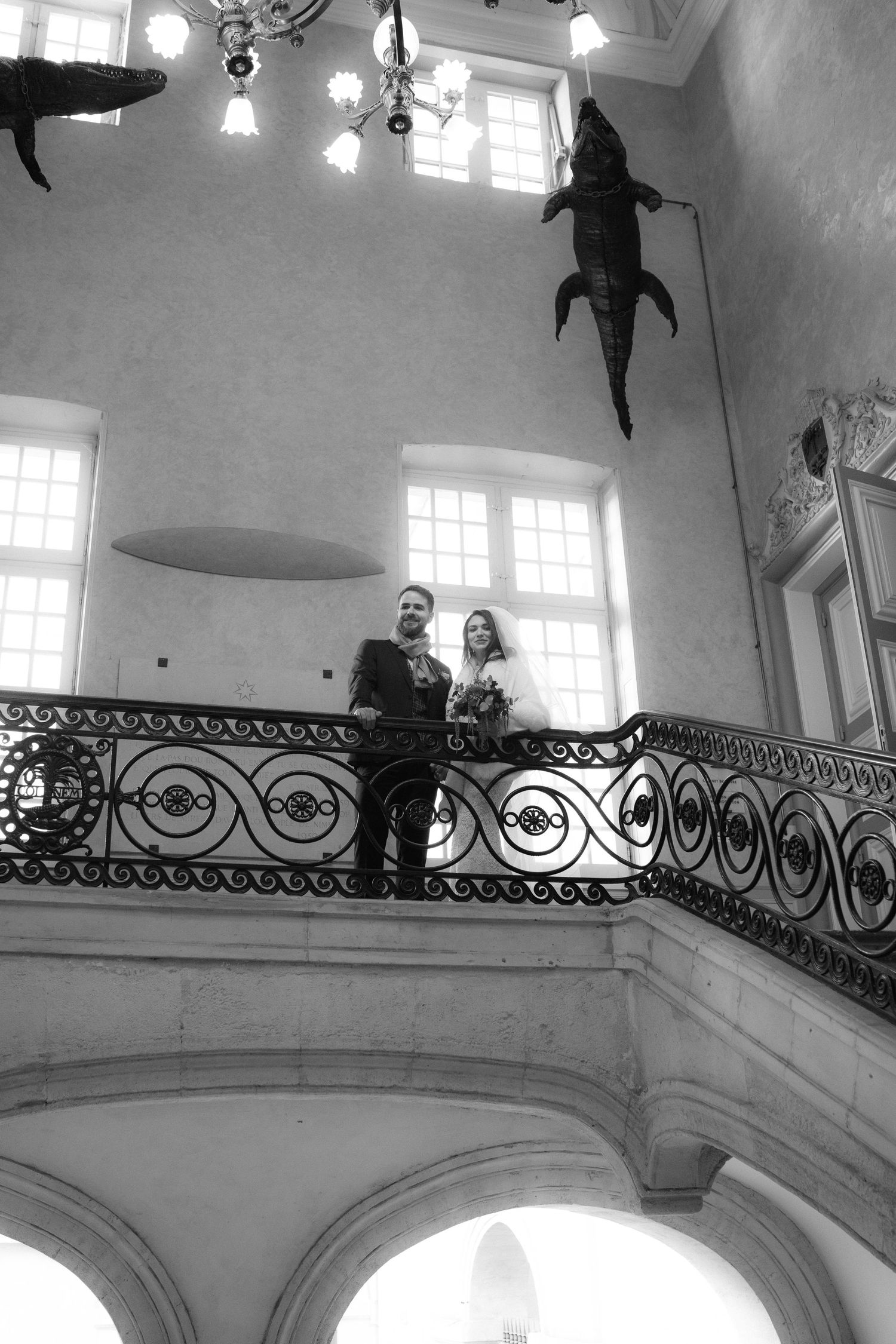 Black and white architectural photograph showing ornate wrought iron railings and arched windows in a grand stairwell.