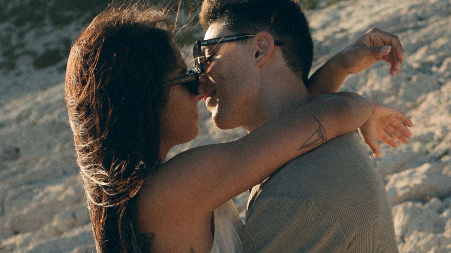 A couple embraces and kisses on a rocky beach at sunset in a series of romantic photographs.