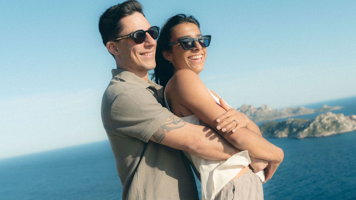 Couple embraces while enjoying scenic coastal views on a sunny day at the beach.