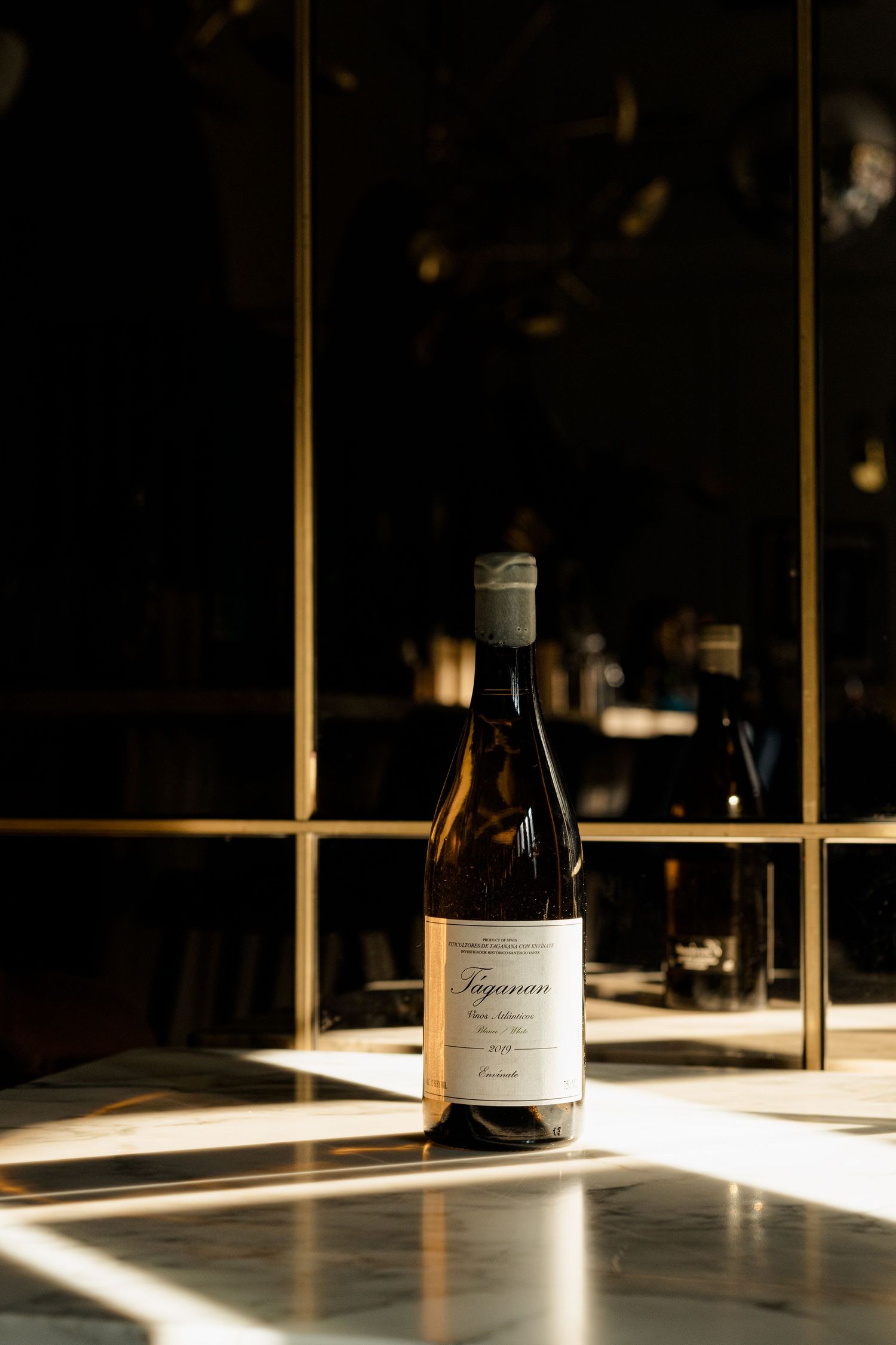 Wine bottle in dramatic lighting against dark background with sunlight streaming through window.