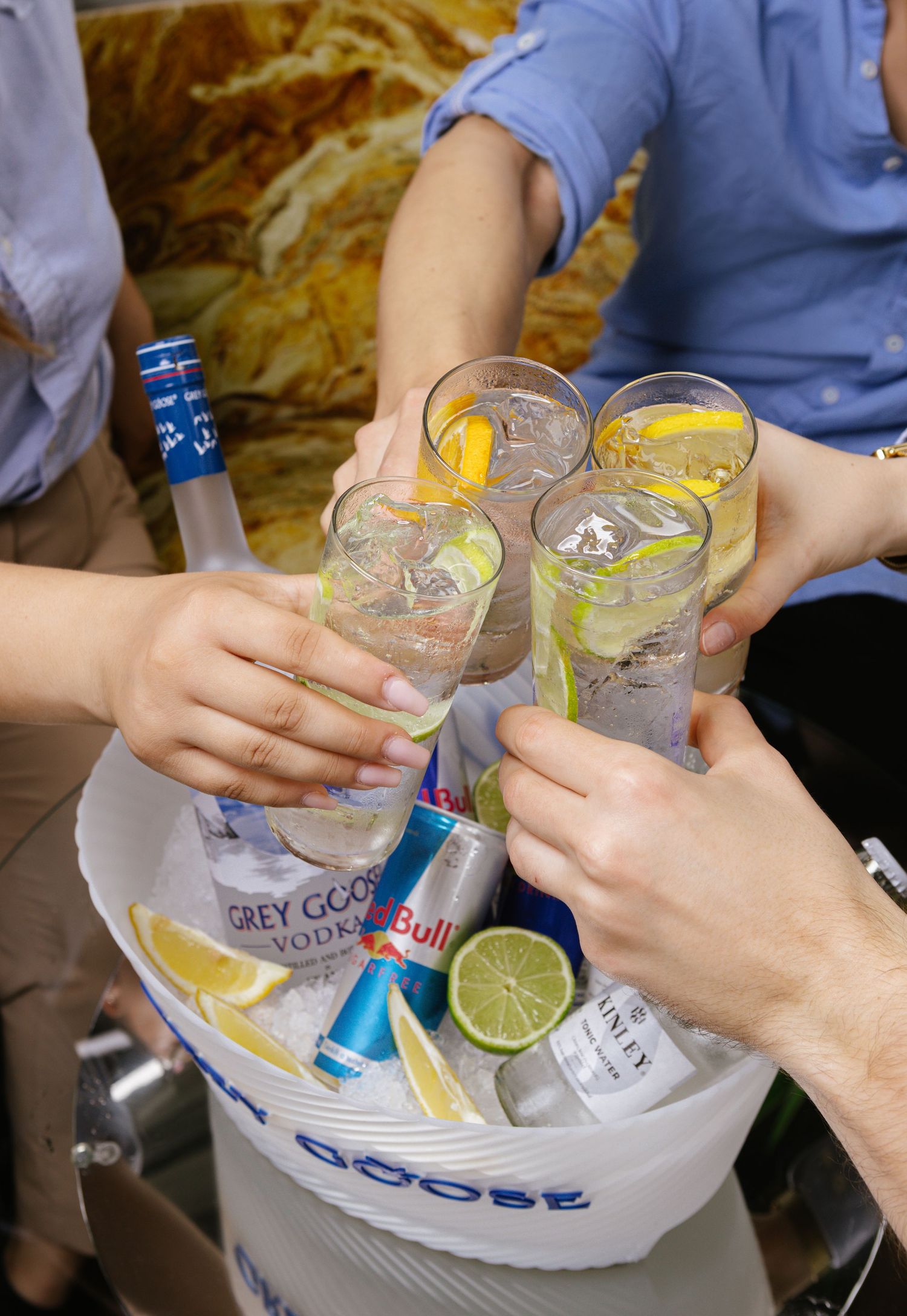 Hands toasting with Grey Goose vodka cocktails garnished with lemon slices.