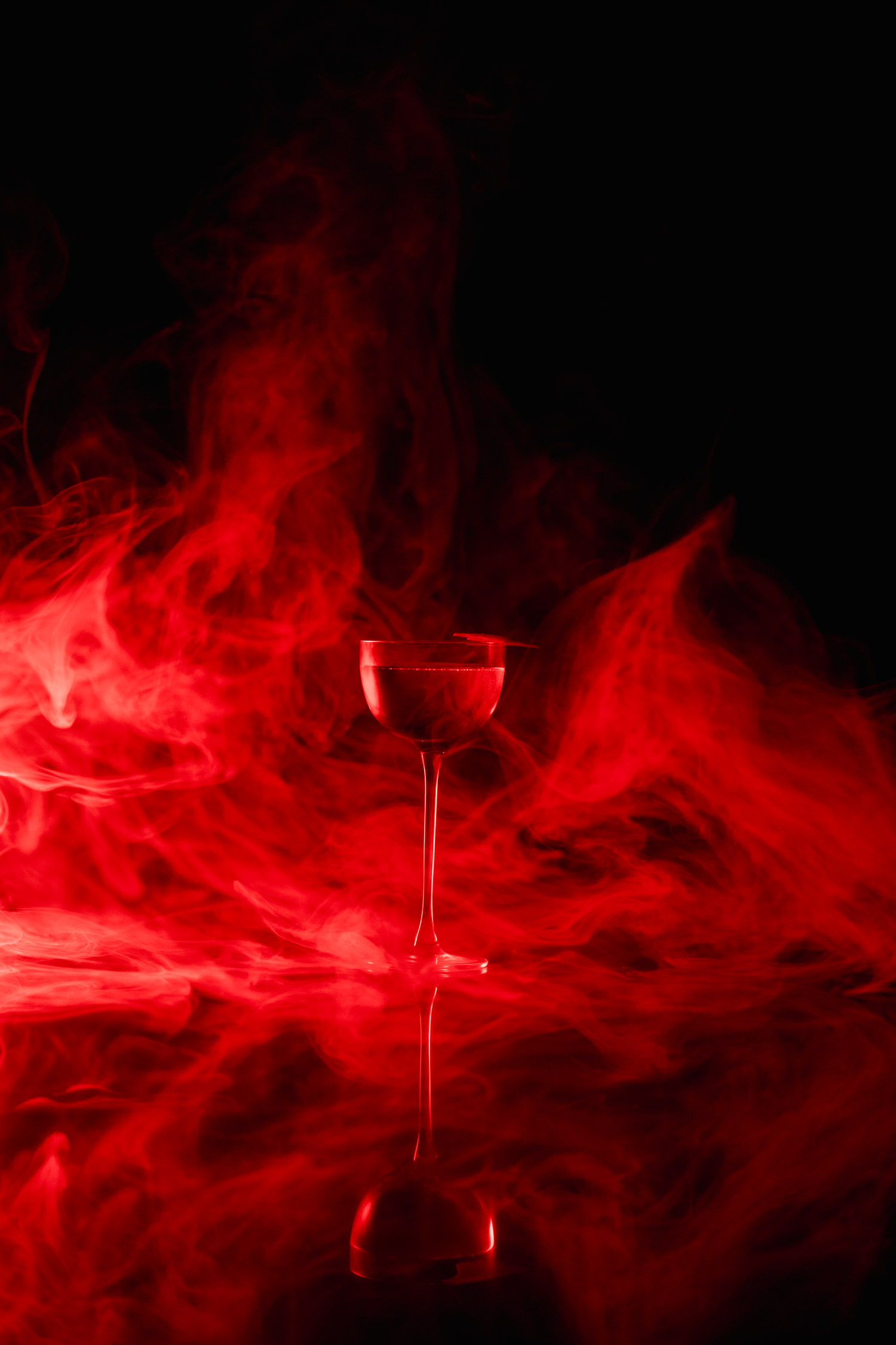 A wine glass silhouetted against dramatic red smoke effects and dark background creates a moody atmospheric scene.