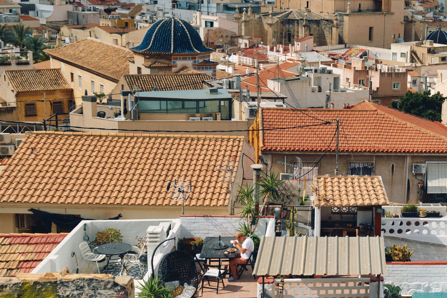 Urban rooftops with domed buildings and terracotta tiles in a Mediterranean coastal city.