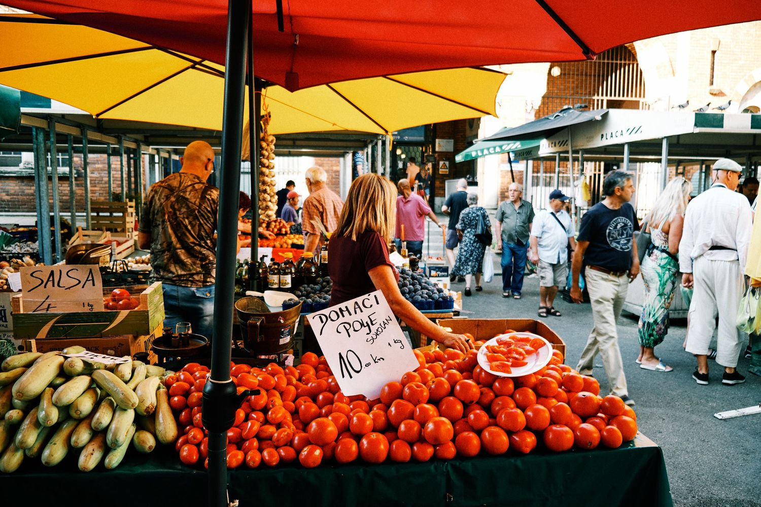 Colorful farmers market stalls with fresh produce and umbrellas on a sunny day.