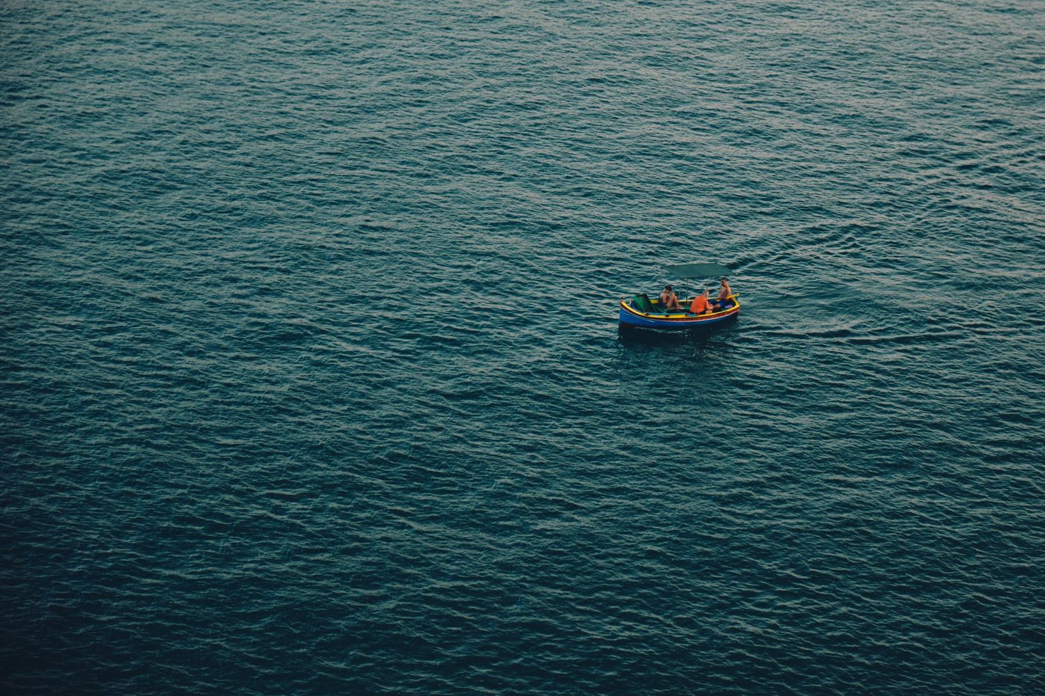 A small boat floating alone on vast blue Mediterranean waters captured from above.
