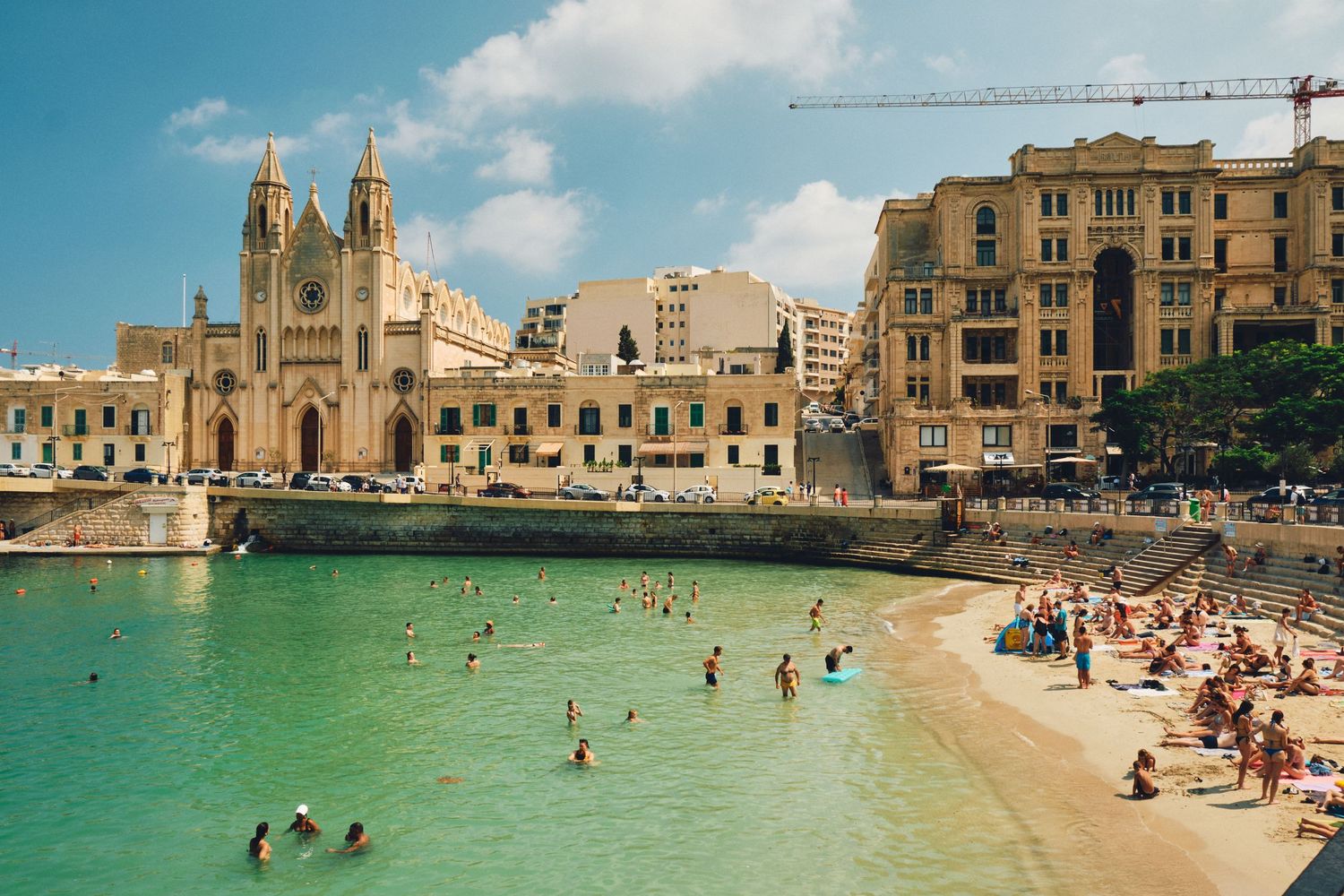 Beautiful beach cove in Malta with historic church and limestone buildings overlooking turquoise Mediterranean waters.
