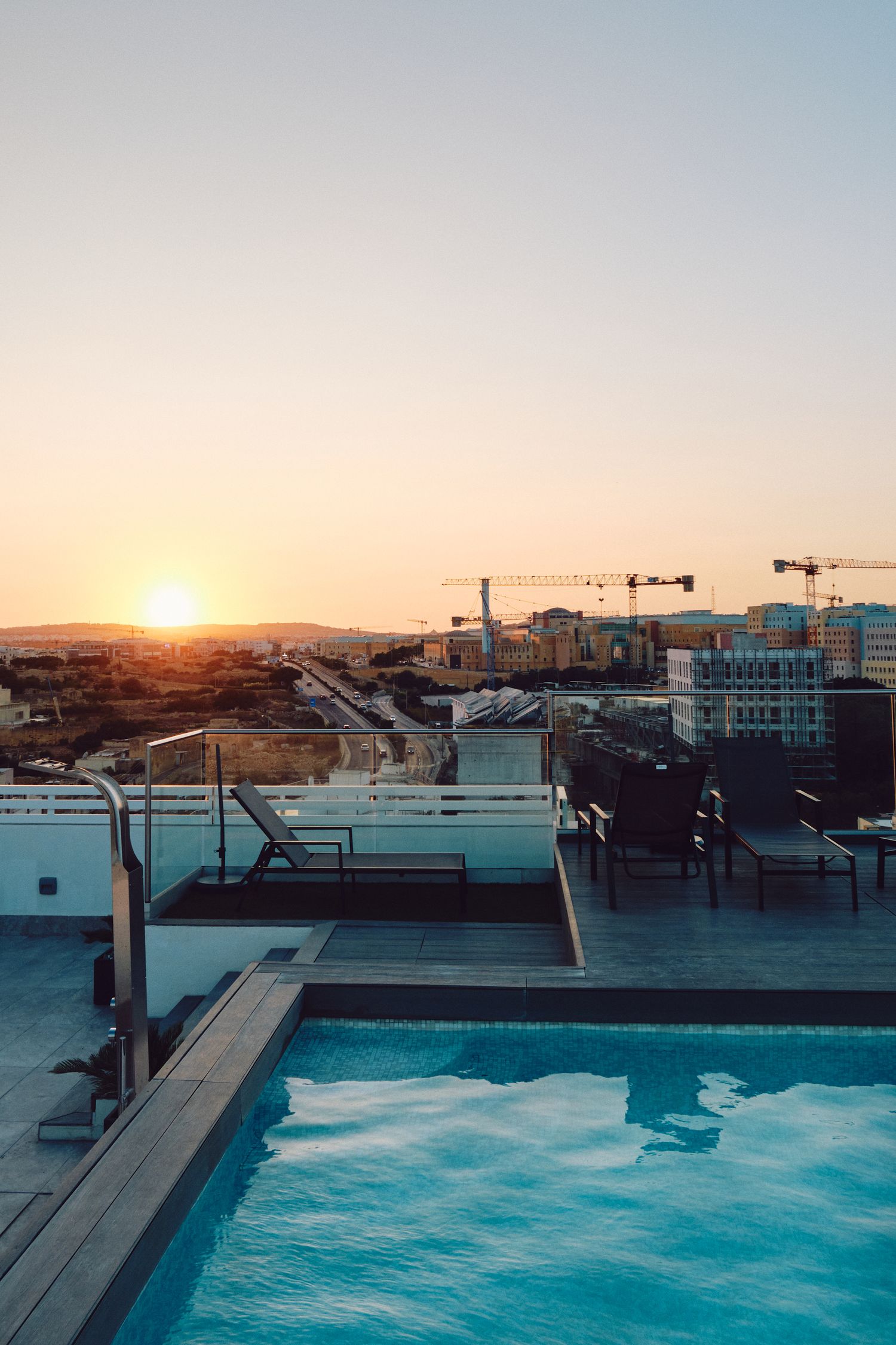 Rooftop infinity pool overlooking city skyline during sunset with construction cranes visible.