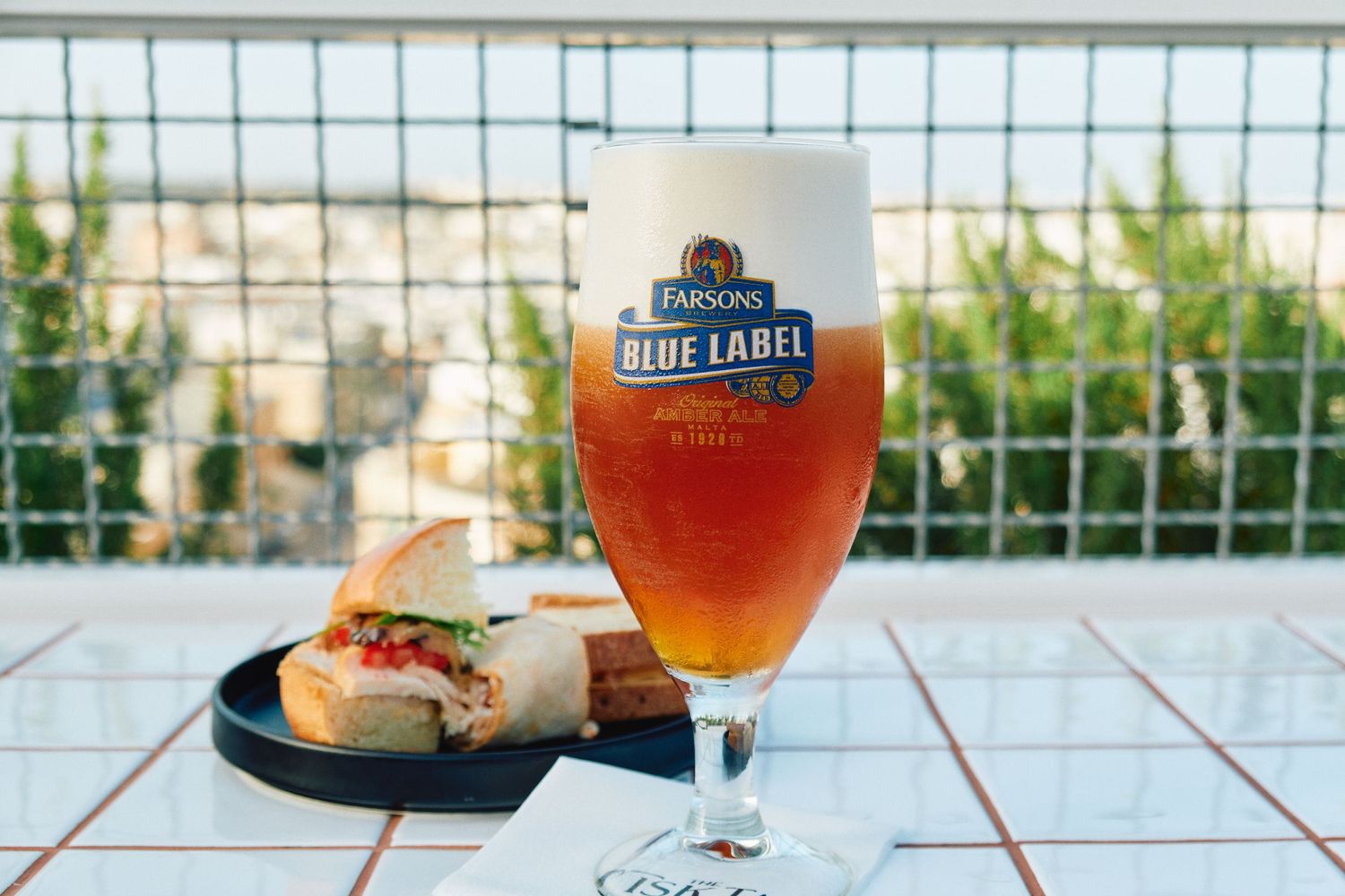 Glass of amber beer and small plate of food on outdoor patio table.