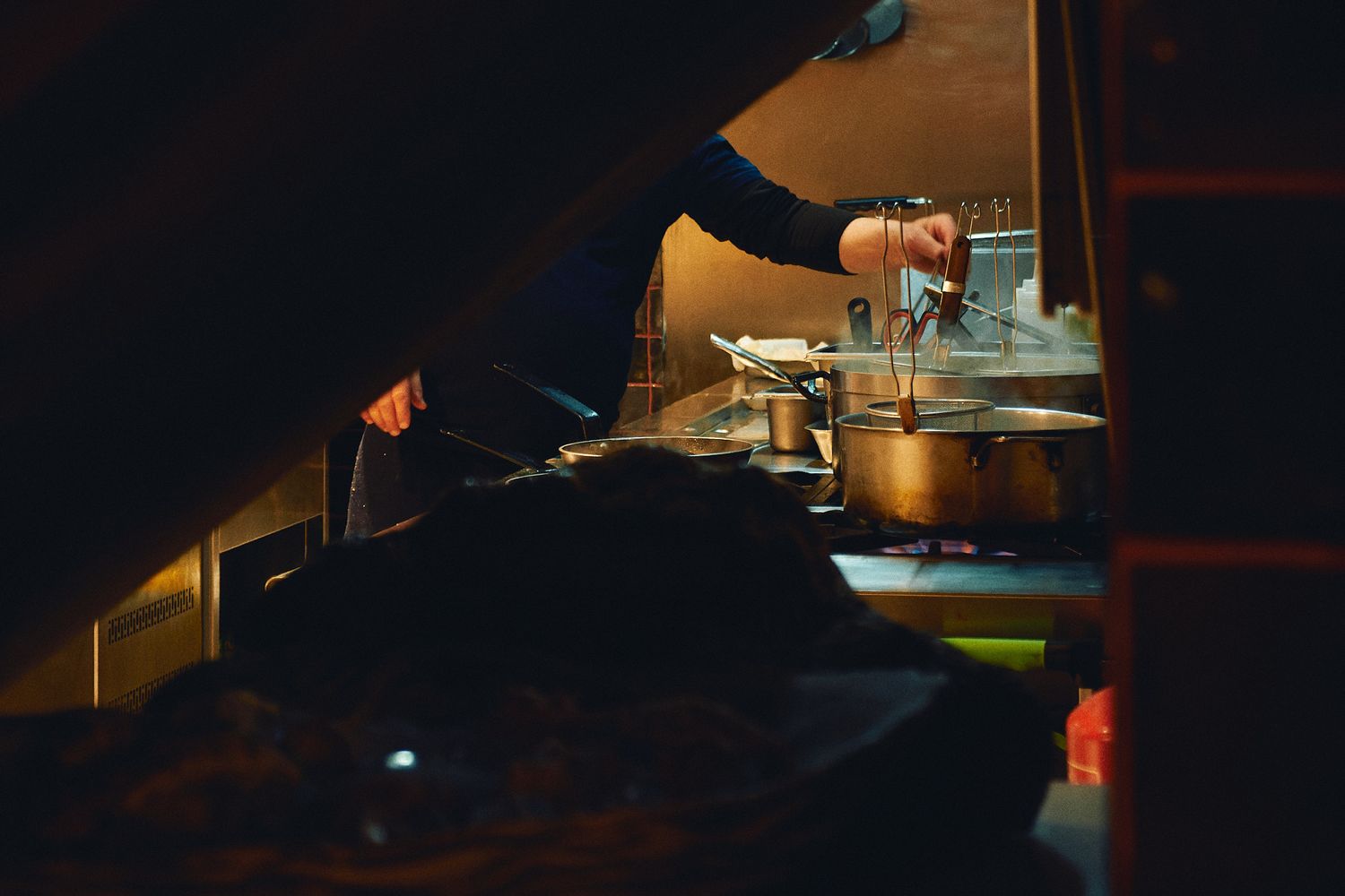 Chef cooking in a dimly lit kitchen with steaming pots and pans on a professional stove.
