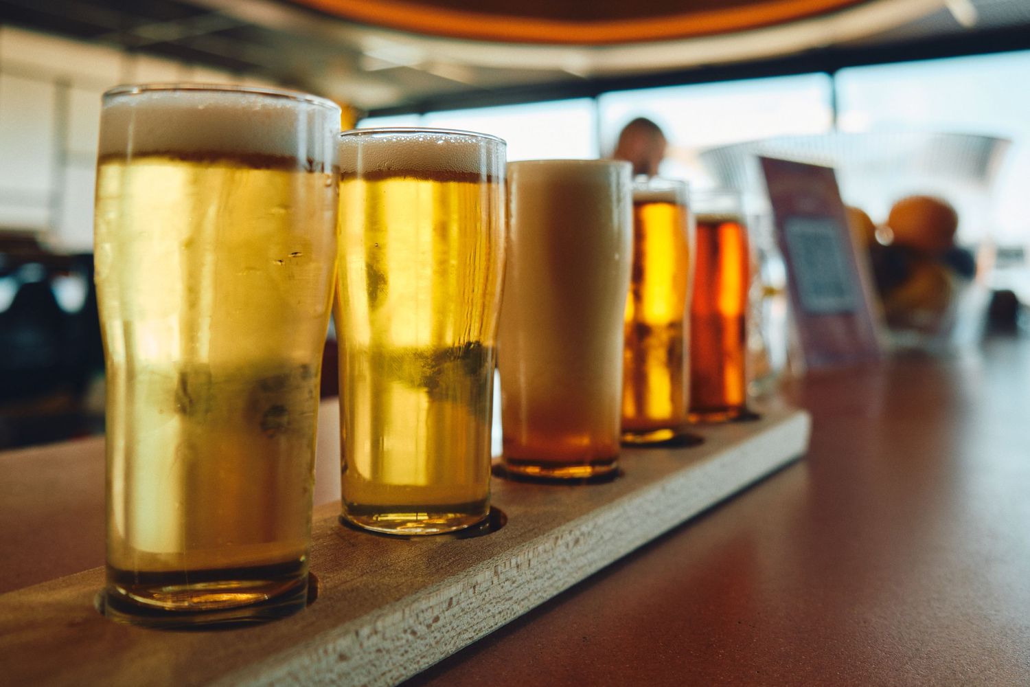Flight of different colored craft beers arranged in a line on a wooden bar counter.