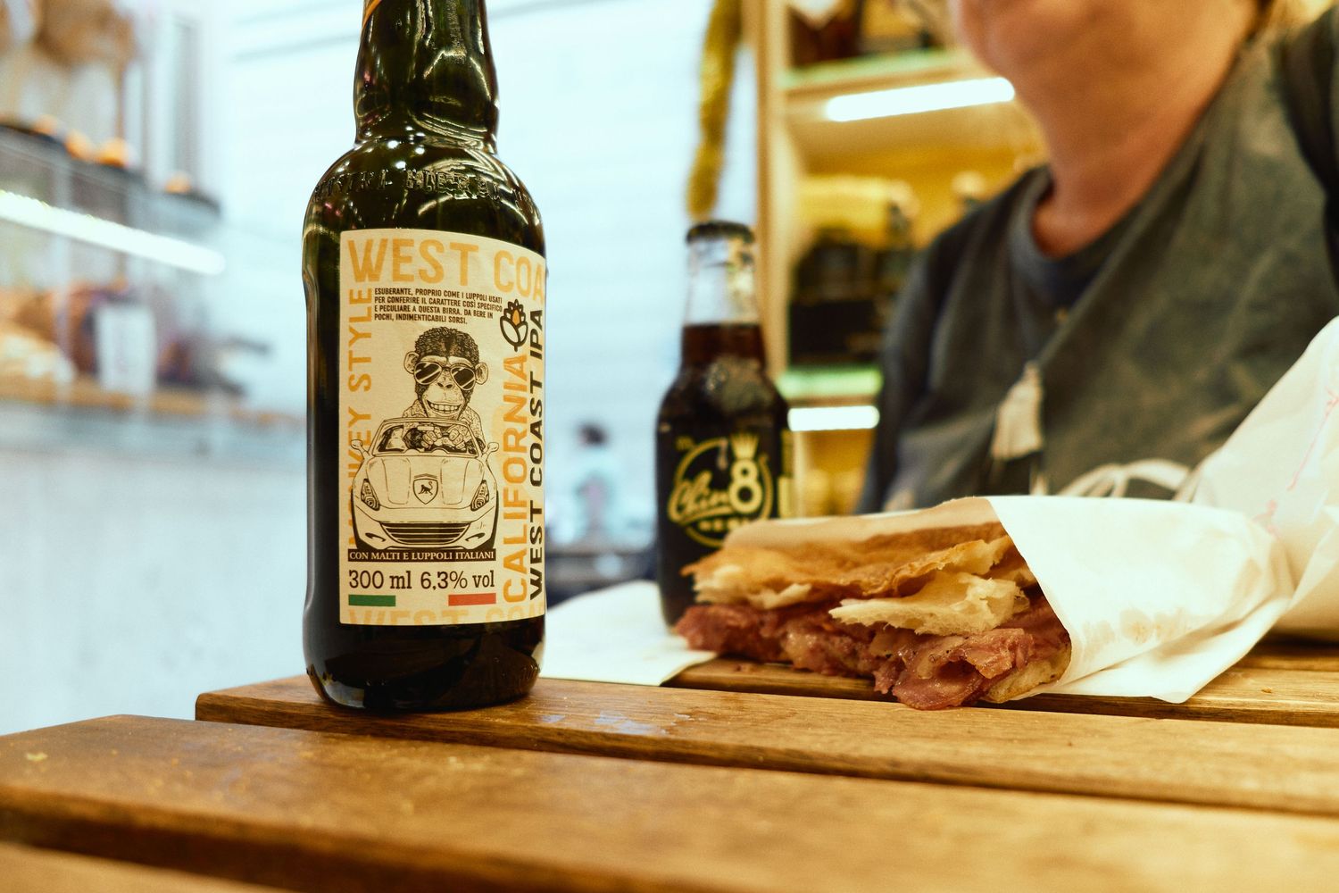 Rustic table setting with artisanal beer bottle and sandwich at an Italian eatery.