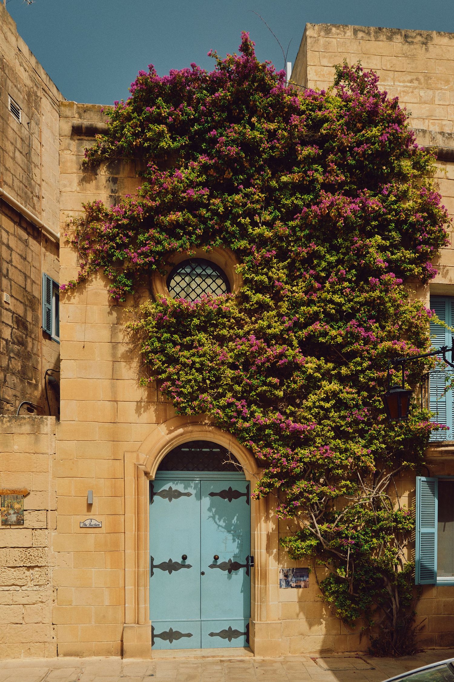 Beautiful blue door framed by pink bougainvillea flowers on honey-colored Mediterranean building.