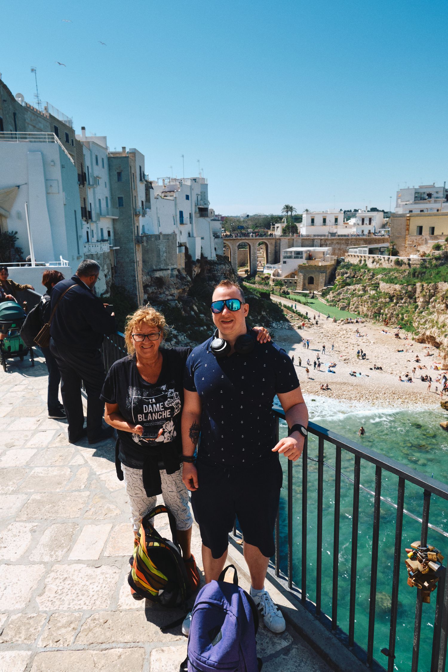 Tourists enjoying the scenic view of a coastal town with white buildings and turquoise waters in Italy.