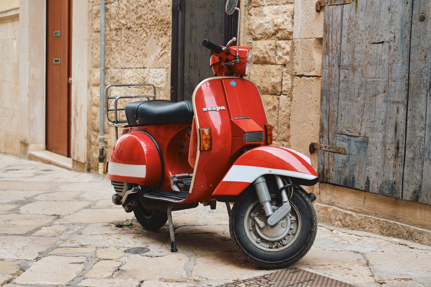 A vintage red Vespa scooter parked on a stone paved street in Italy.