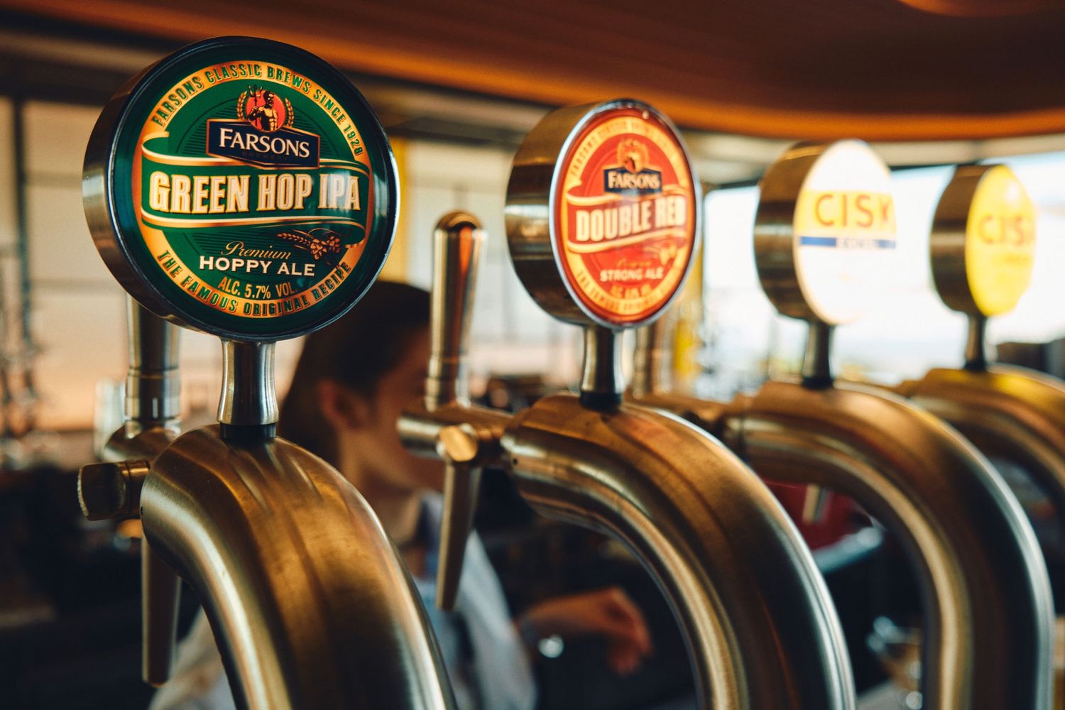 Row of beer tap handles at a bar featuring different brewery labels and logos.