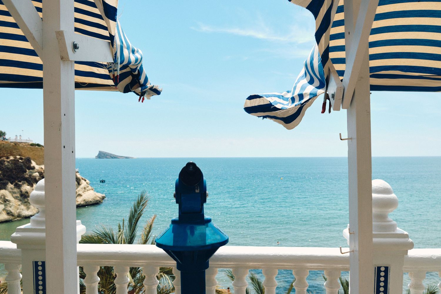 Seaside balcony with blue and white striped awnings framing ocean view.