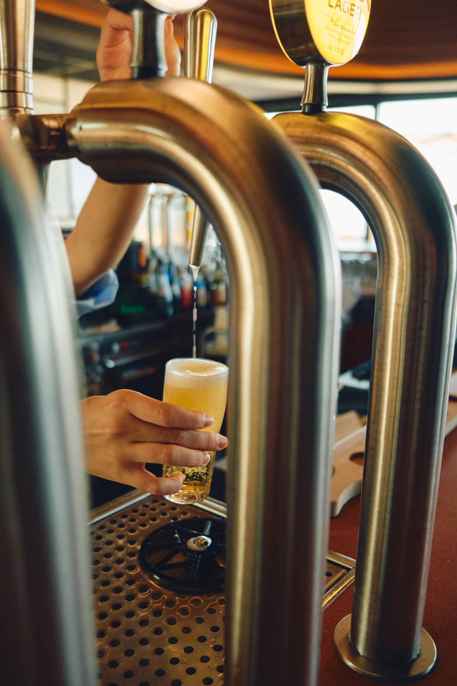 Beer being poured from a chrome draft tap into a glass at a bar.