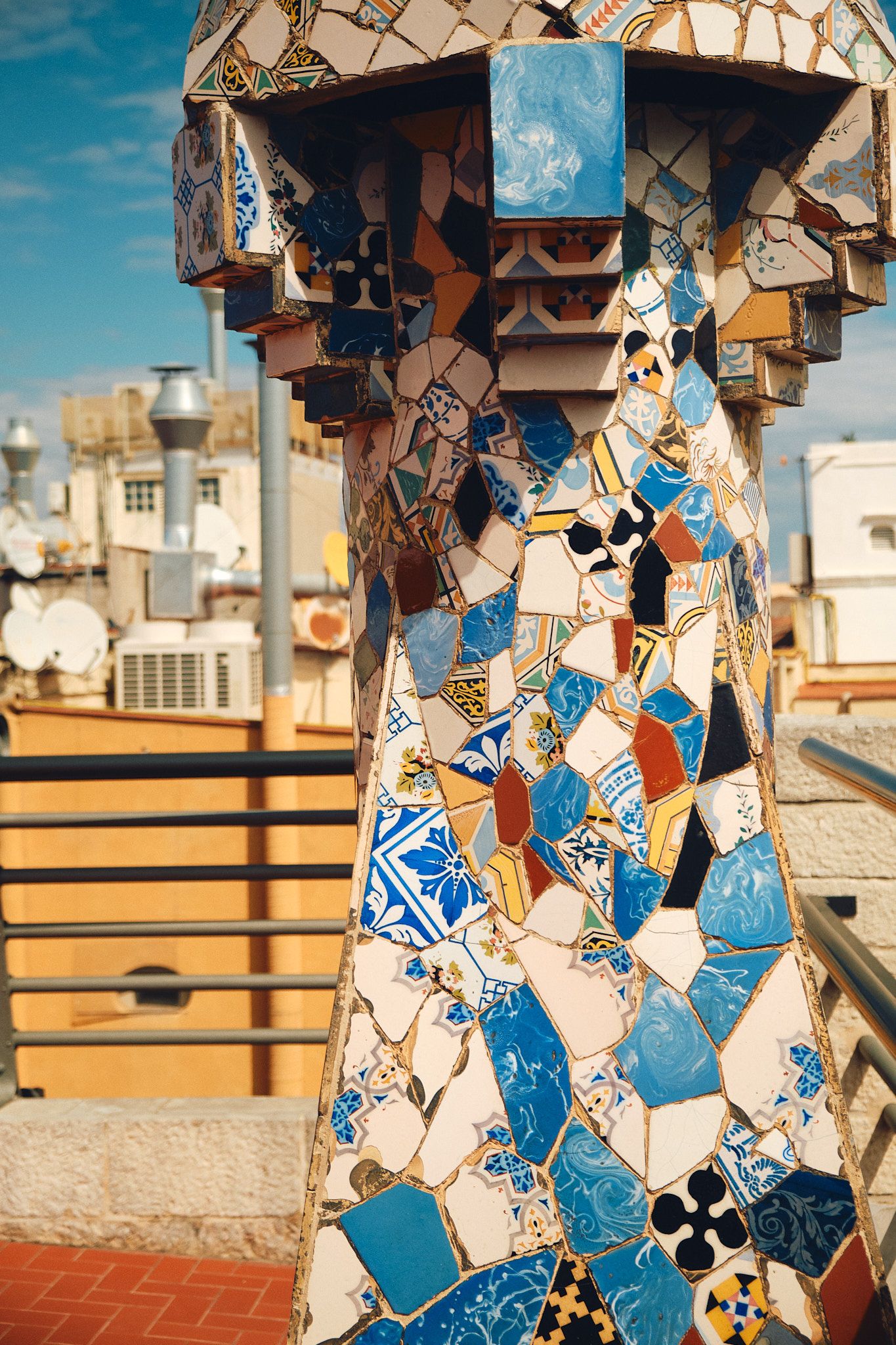 Colorful mosaic chimney at Casa Batllo rooftop in Barcelona, featuring intricate ceramic tile patterns in blue and white.