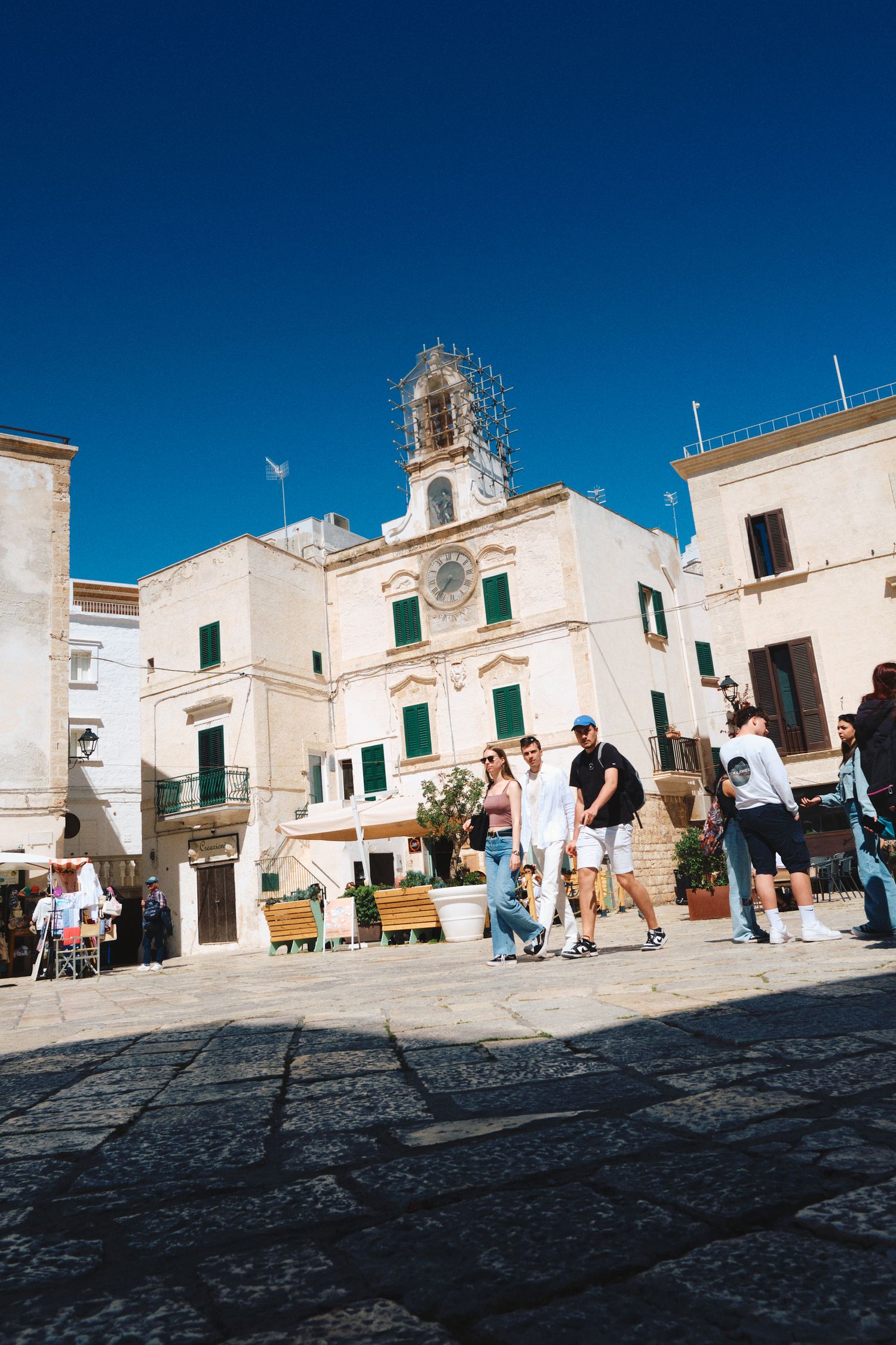 Historic white church and buildings in an Italian town square with tourists walking by.