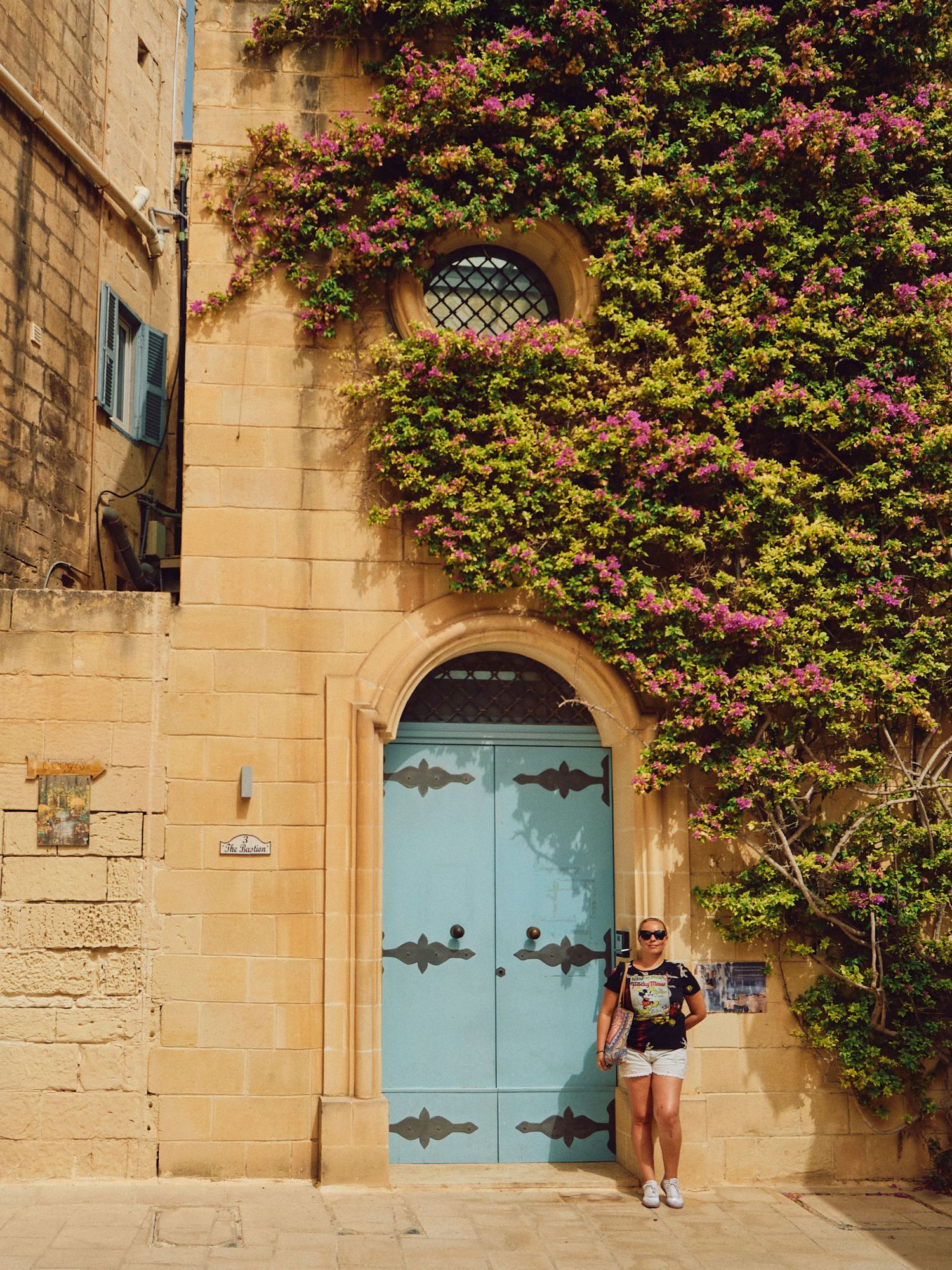 Historic Mediterranean building with turquoise door covered in climbing pink bougainvillea.