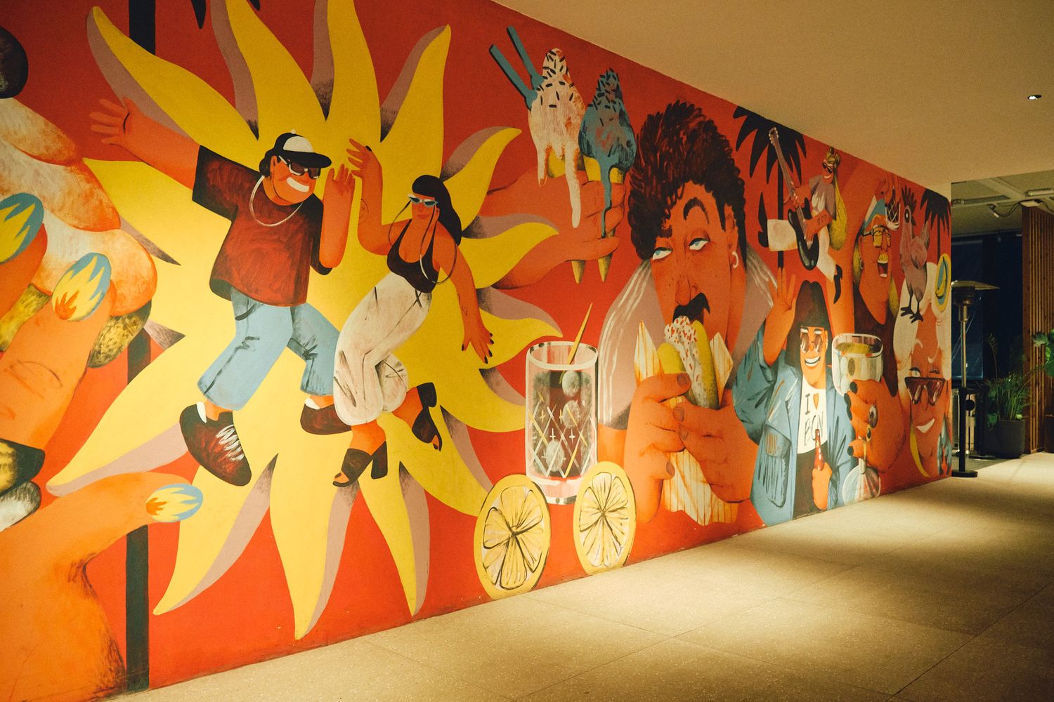 Colorful large-scale mural featuring vibrant figures dancing and celebrating on an orange and yellow wall in a modern hallway.