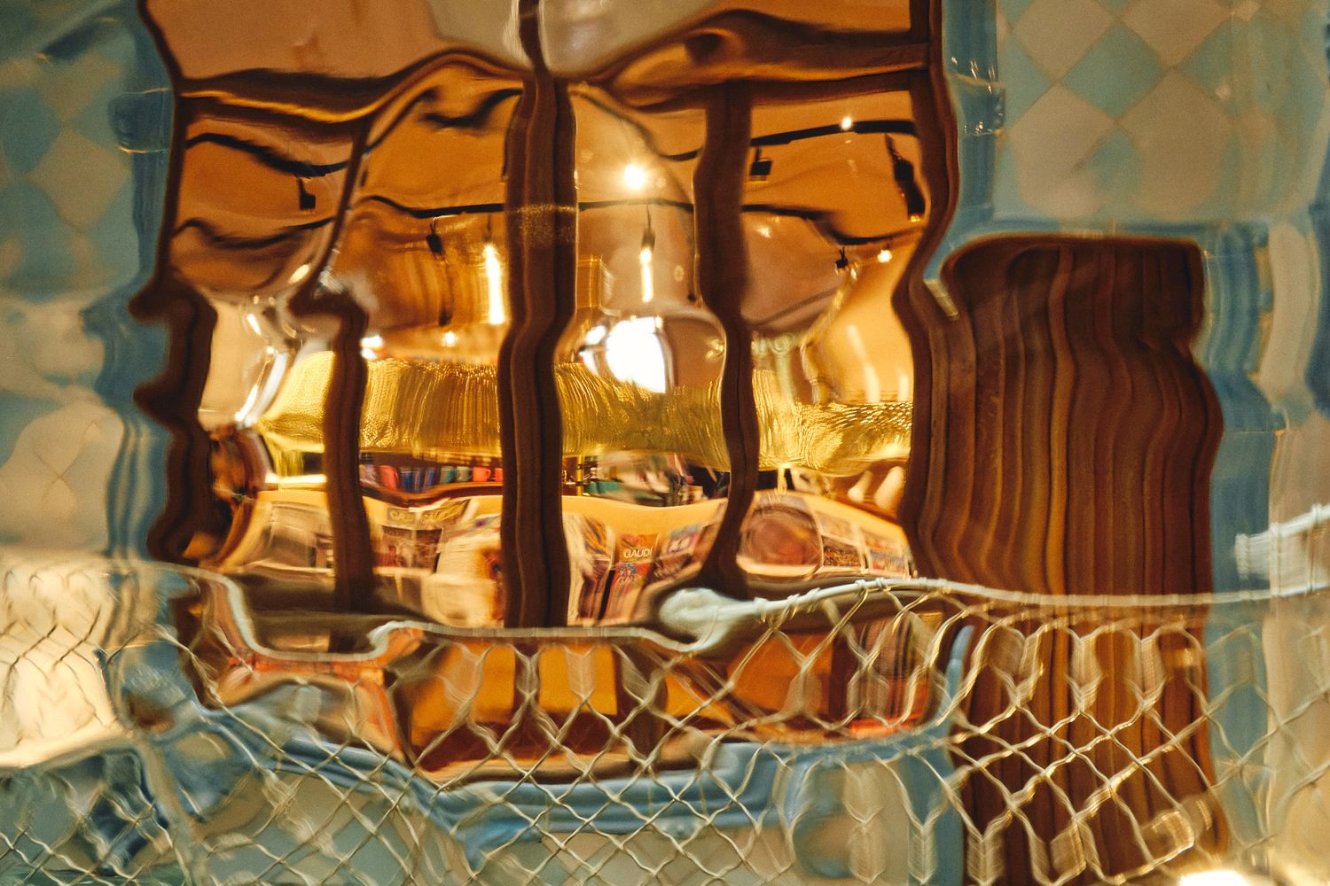 Abstract reflection through wavy glass window revealing warm golden interior with ornate details at Casa Batlló, Barcelona.