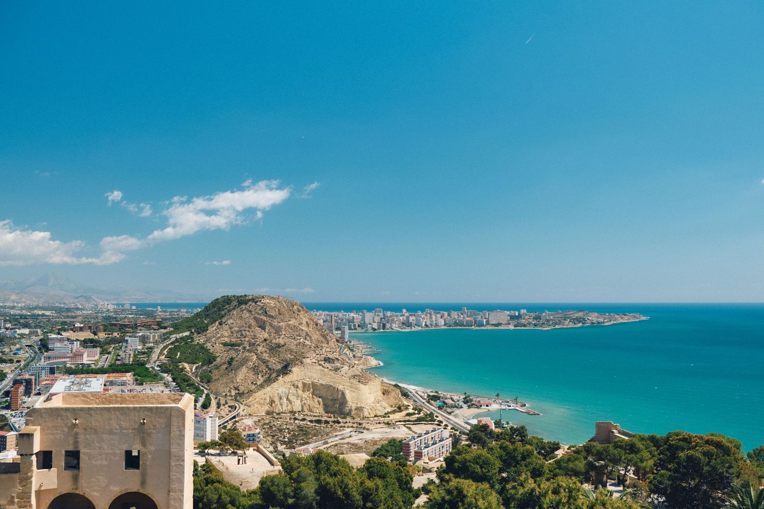 Coastal Mediterranean cityscape with turquoise waters and mountain backdrop.