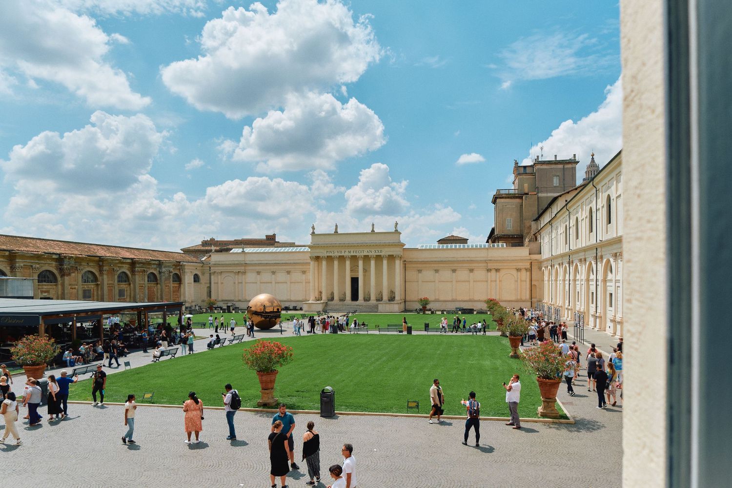 Green courtyard surrounded by Vatican museum buildings with tourists walking around.