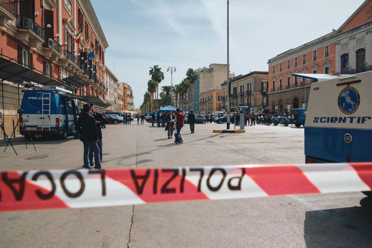 Urban street blocked by police tape with emergency vehicles and pedestrians in background.
