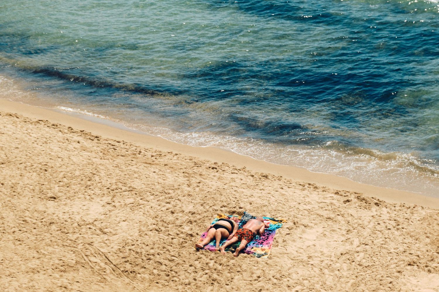 Two beach towels laid out on golden sand next to turquoise ocean waters on a sunny day.