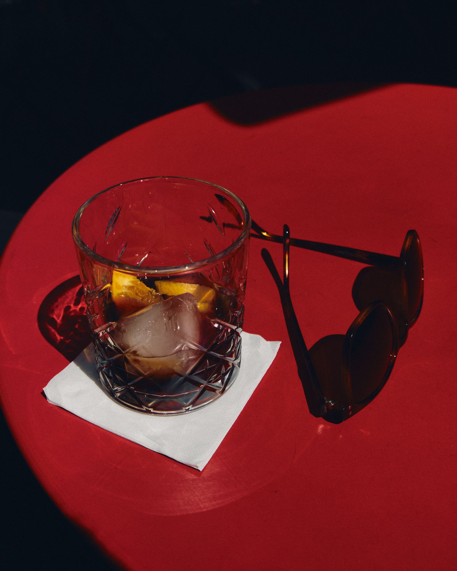 Whiskey glass casting a dramatic shadow on a red table surface.