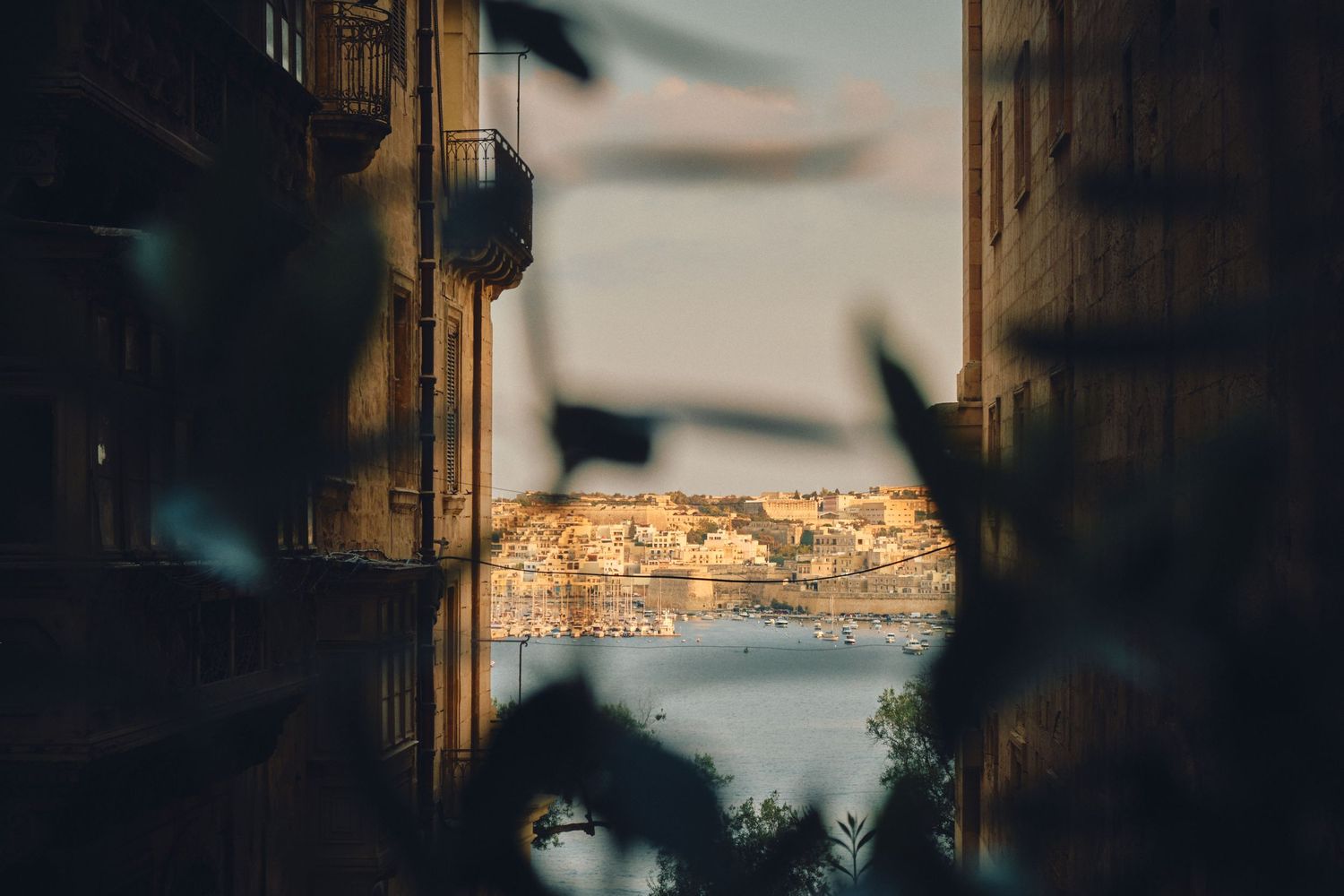 A scenic view of a Mediterranean coastal town framed between buildings with golden sunlight illuminating the architecture.