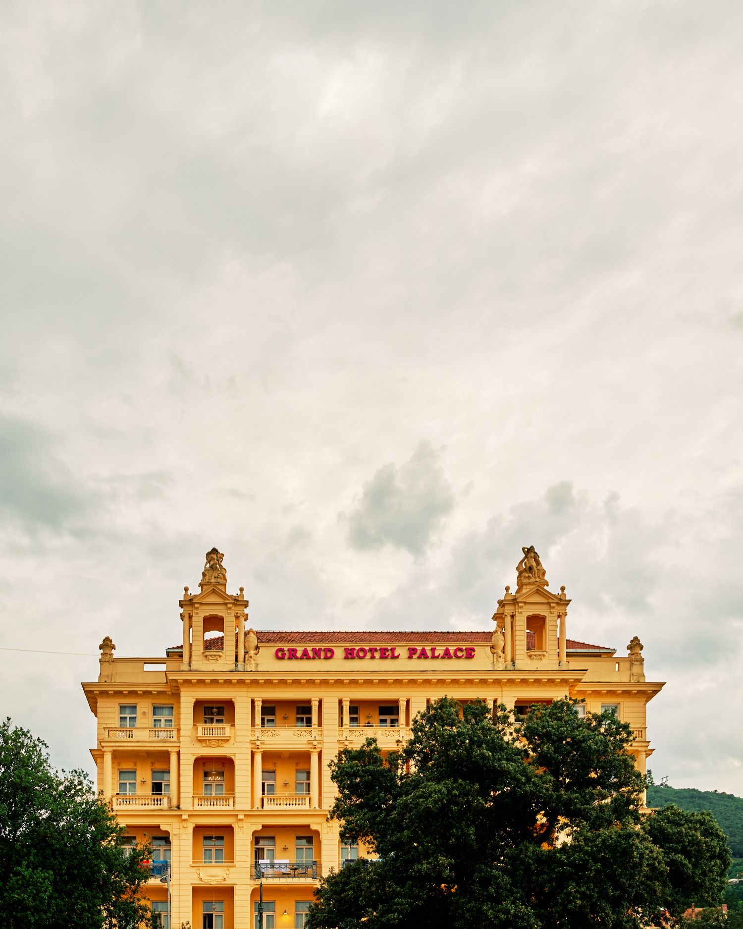 Grand Hotel Palace building with ornate yellow facade against cloudy sky.