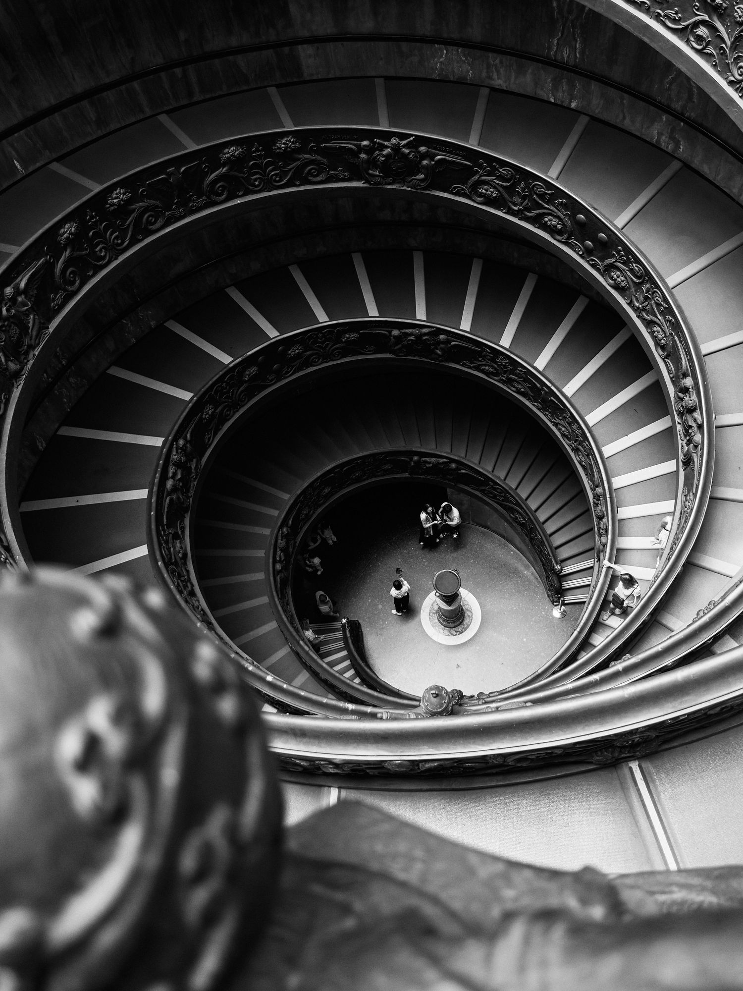 Aerial view of a spiral staircase in black and white with ornate railing at the Vatican Museums.