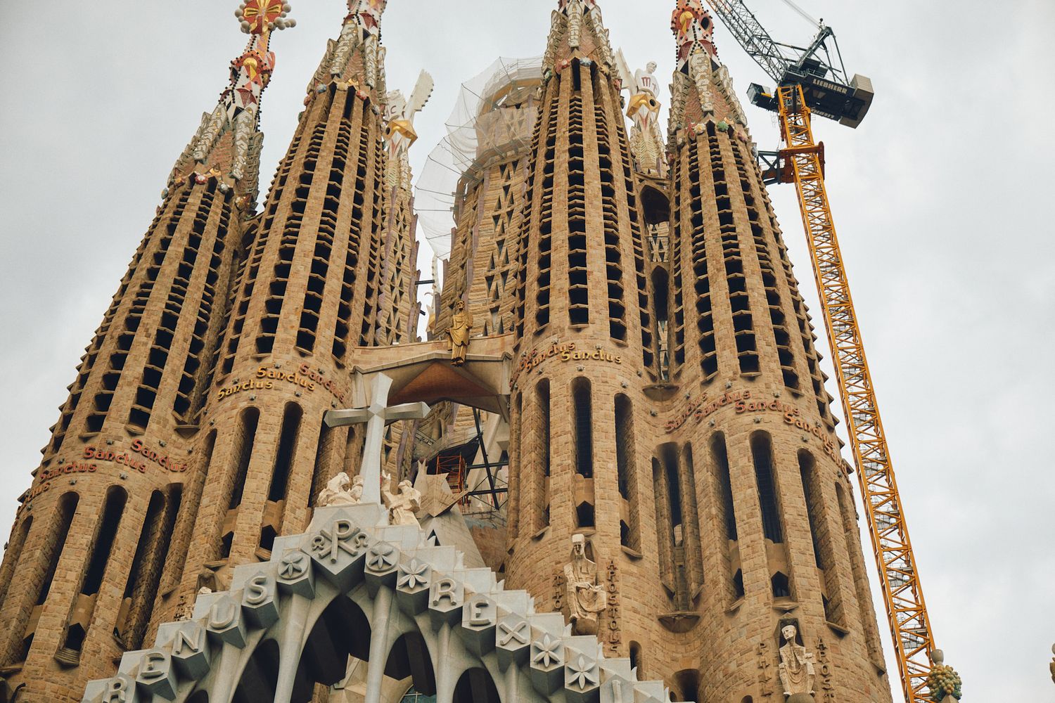 Sagrada Familia basilica in Barcelona with ornate stone spires and a construction crane under cloudy skies.