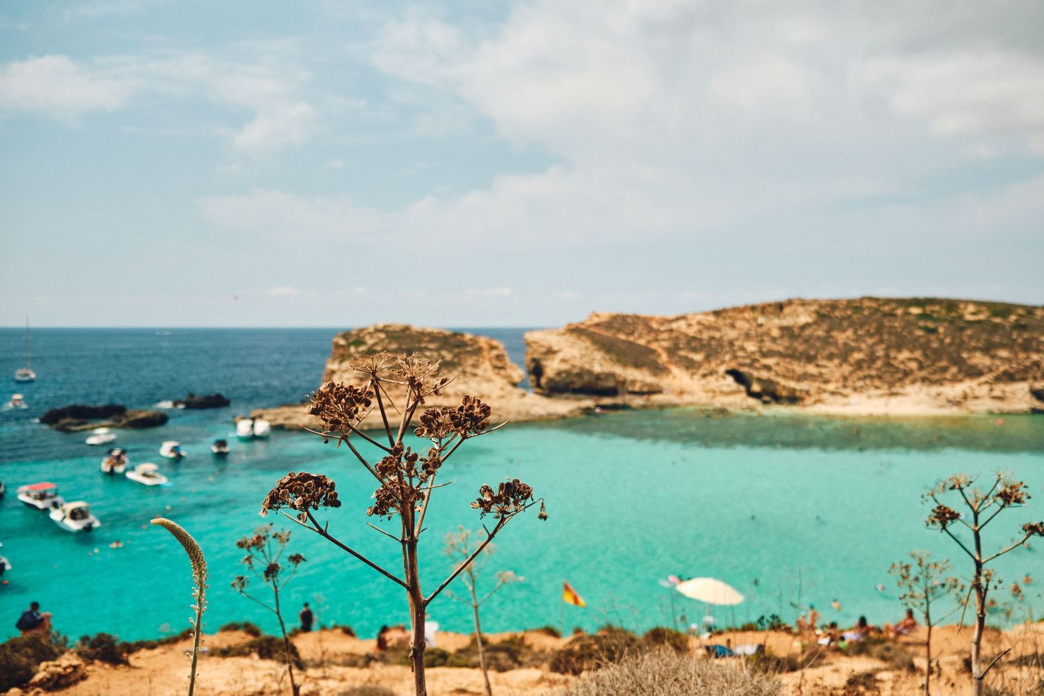 Crystal clear turquoise waters of Malta's Blue Lagoon with boats anchored near rocky cliffs.