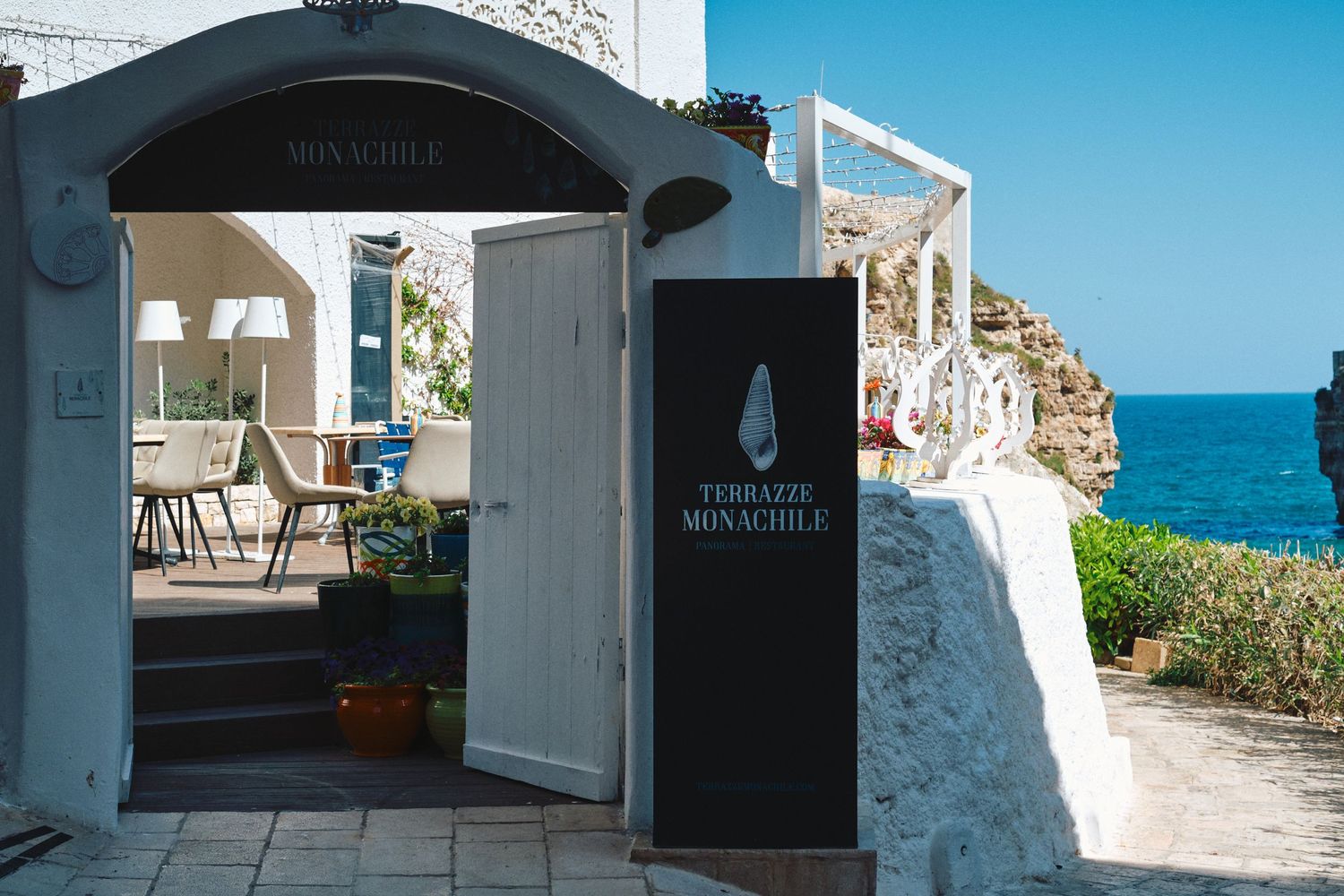 Elegant seaside restaurant entrance with white walls and blue signage overlooking the ocean.