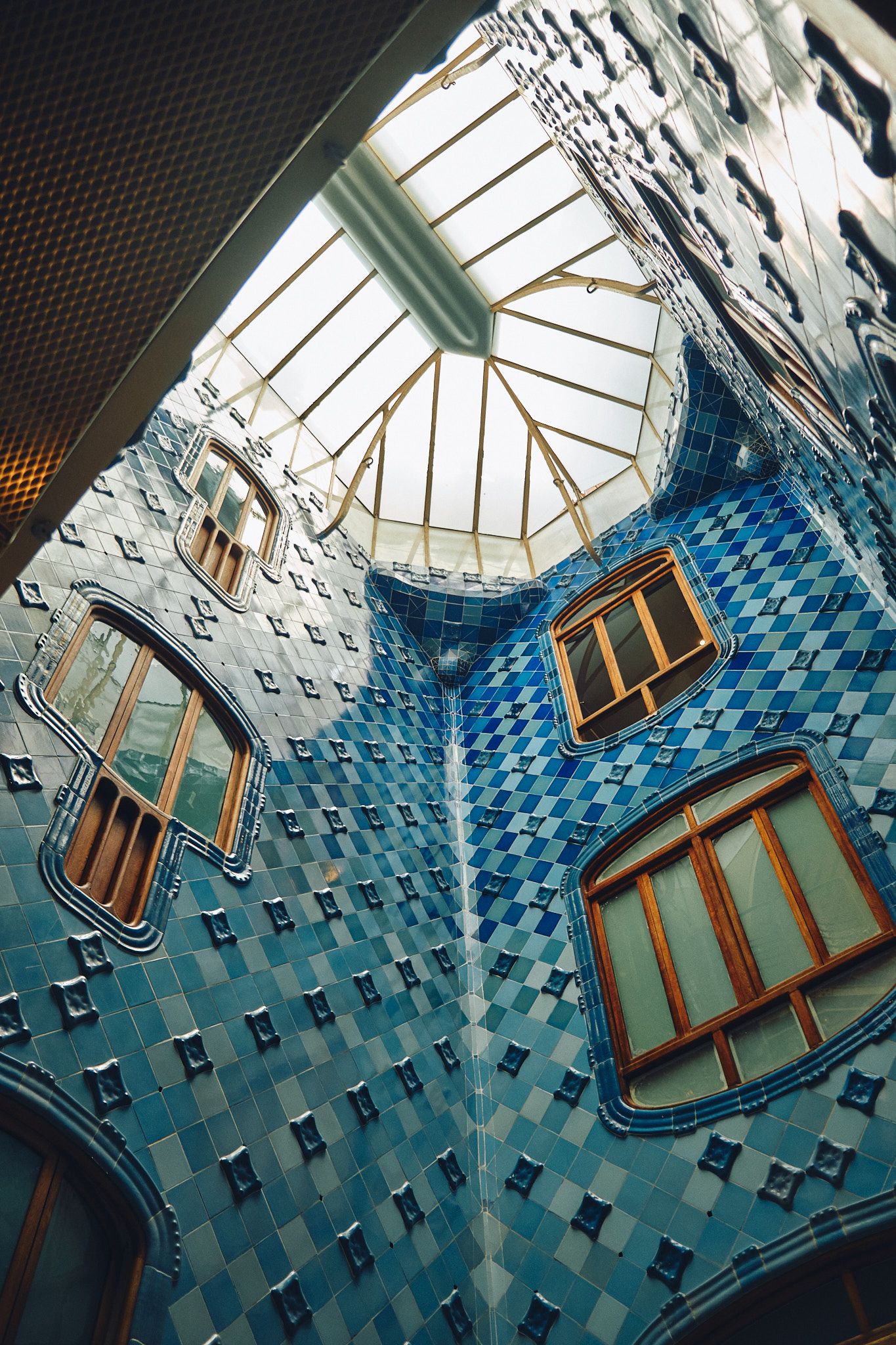 Interior courtyard of Casa Batlló by Gaudí, featuring blue mosaic tiles and organic-shaped windows in Barcelona.