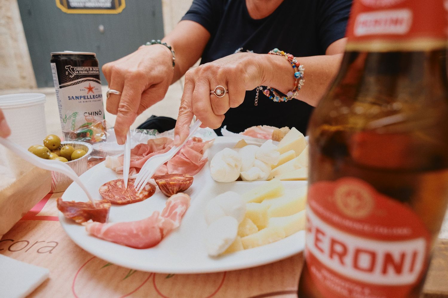 A close-up of hands serving charcuterie and cheese alongside a Peroni beer bottle on a plate.