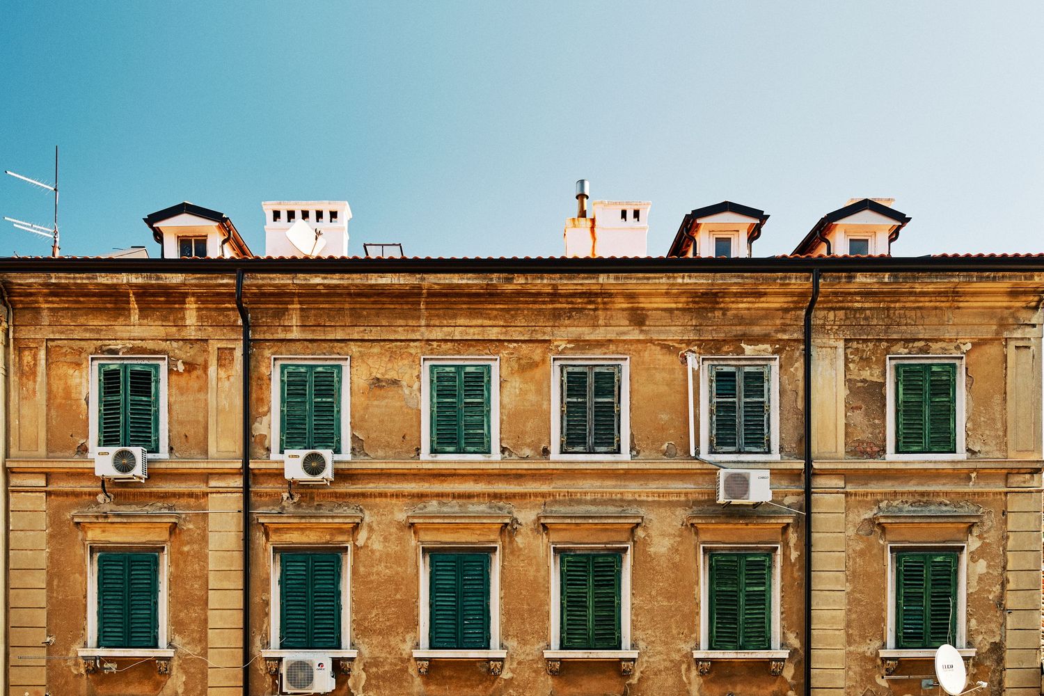 Historic yellow apartment building with green shuttered windows and Mediterranean architecture.