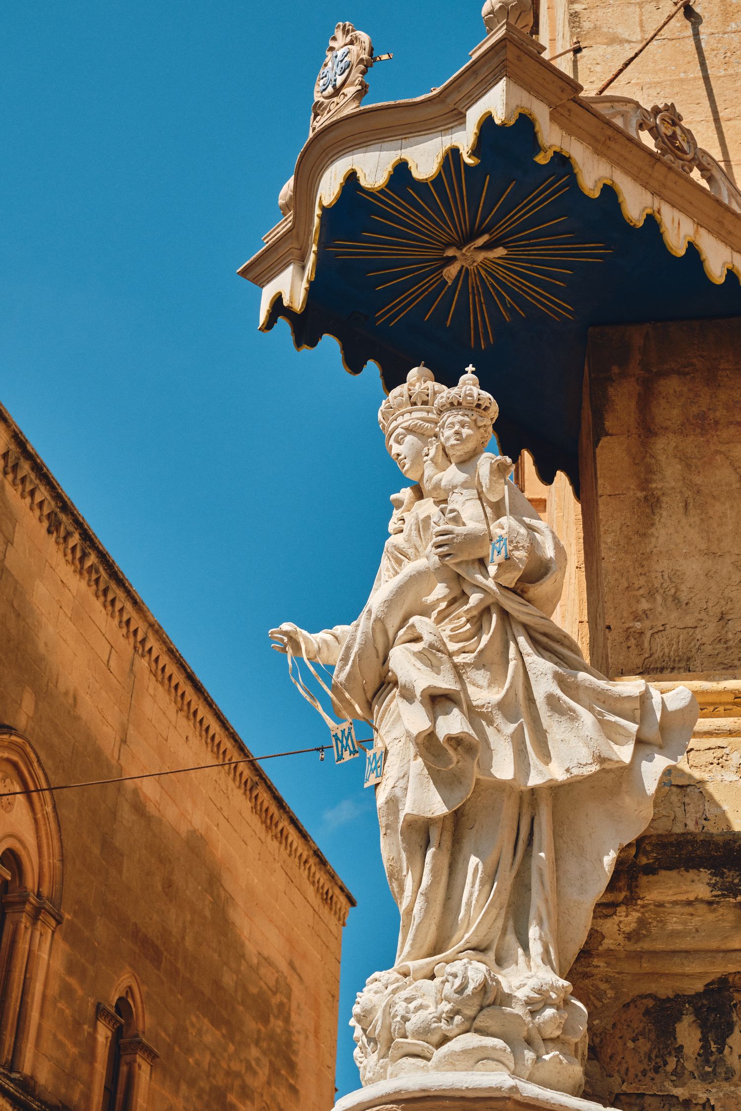 Ornate white stone statue under a decorative canopy against bright blue sky on historic building facade.