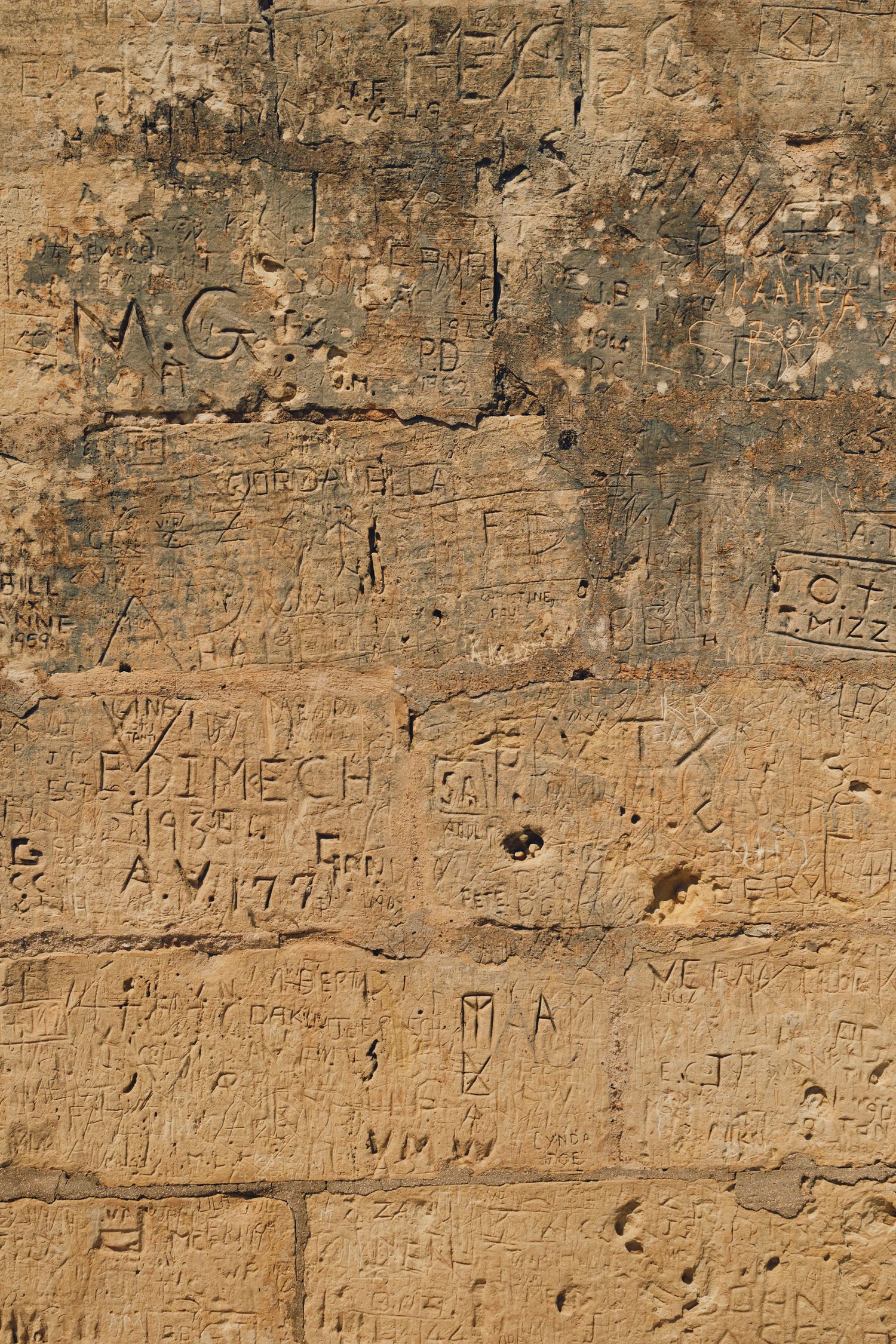 Ancient stone wall covered in weathered graffiti and inscriptions.